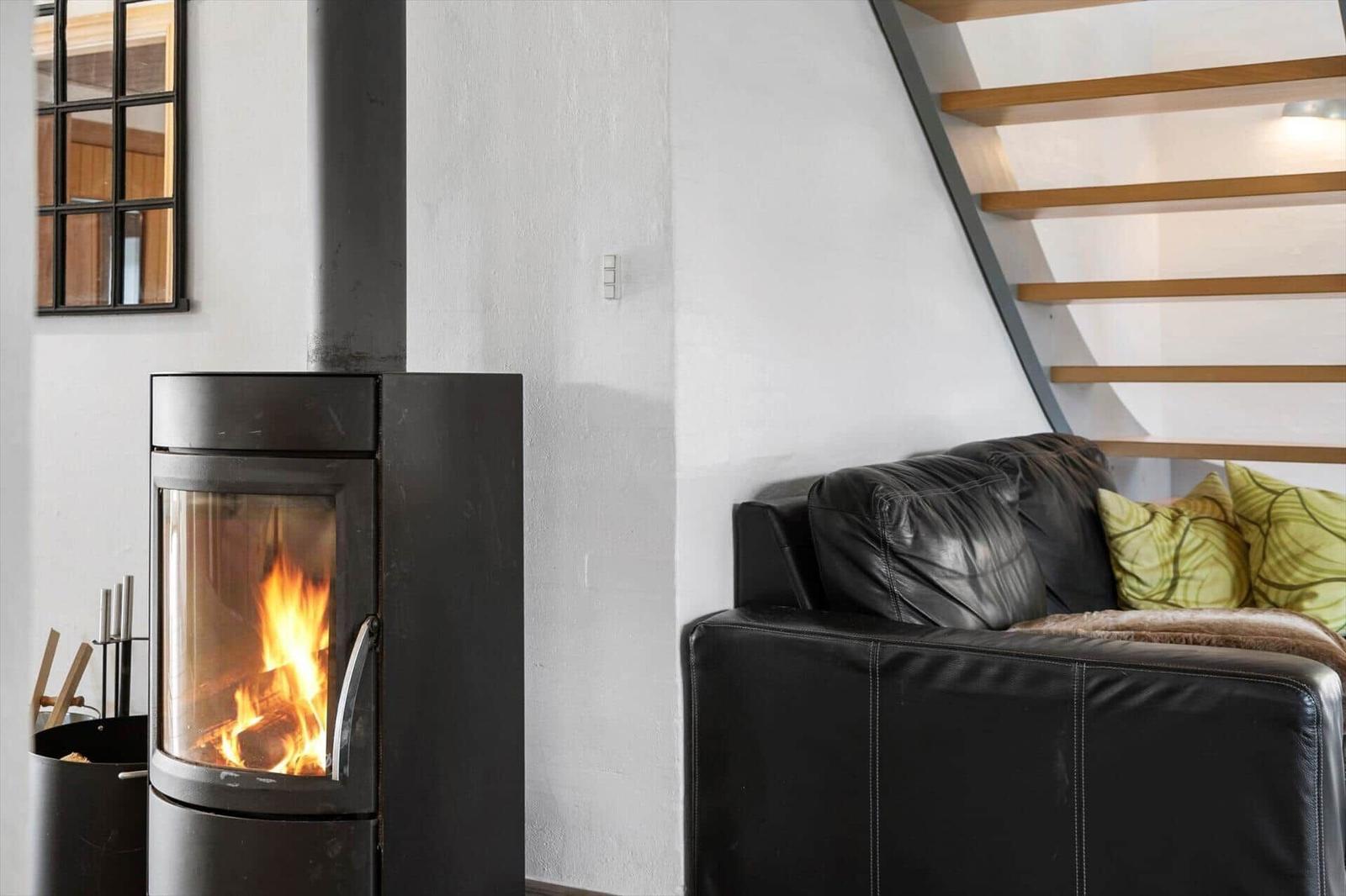 Black wood-burning stove, black leather sofa with green cushions, wooden staircase.