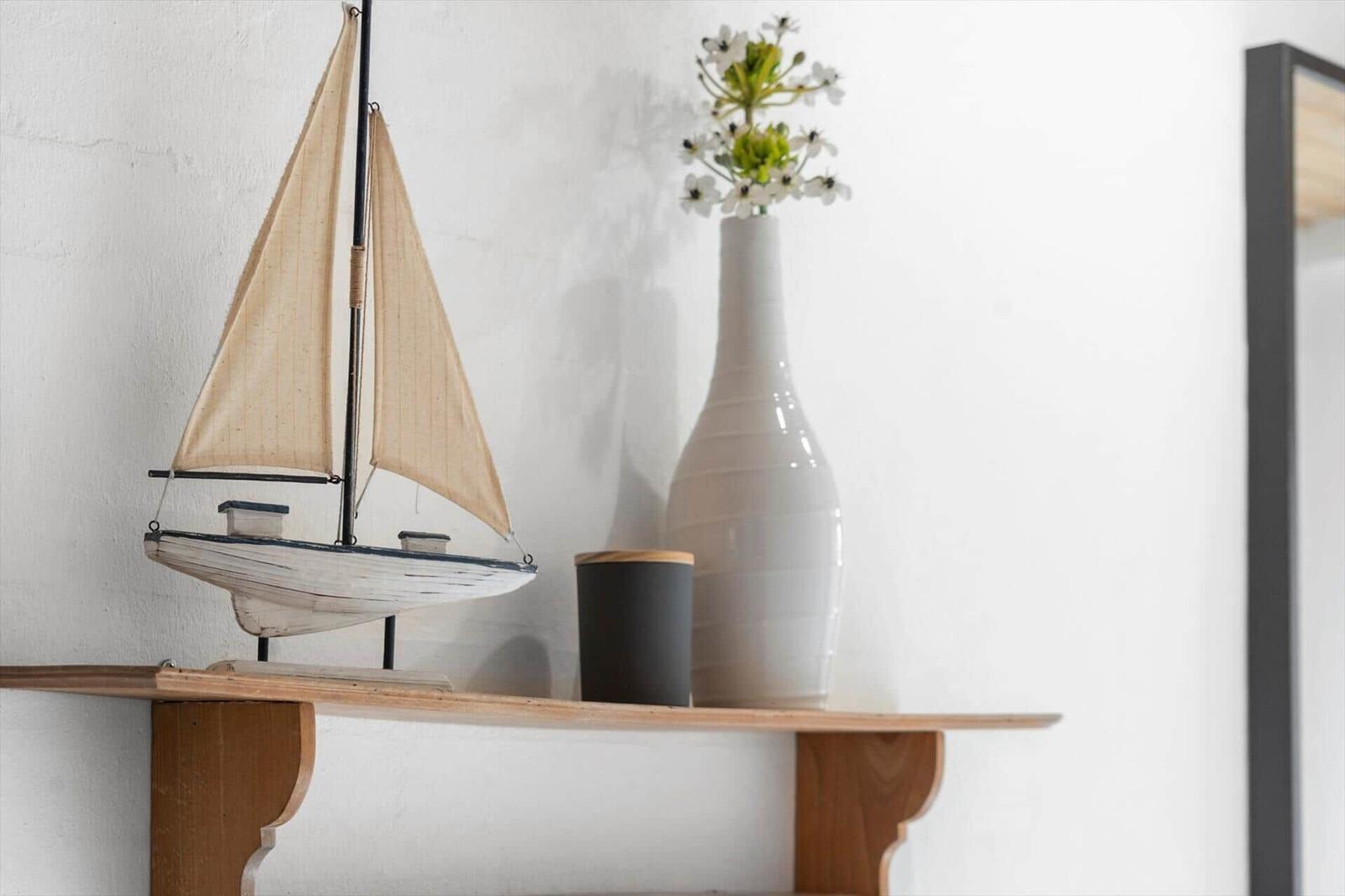 A model boat and a vase with flowers are on a wooden shelf.