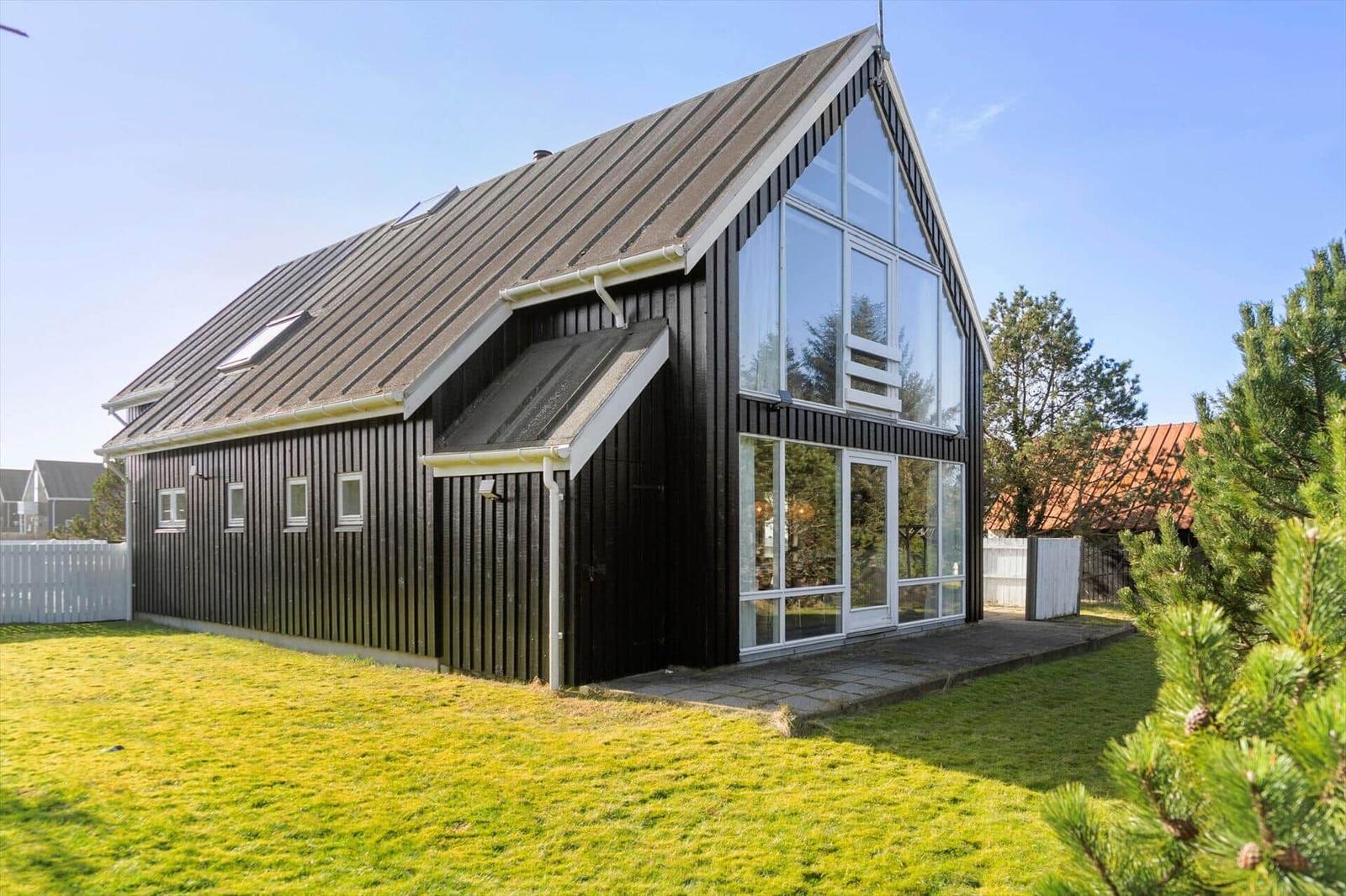 Modern wooden house with large glass area and lawn.