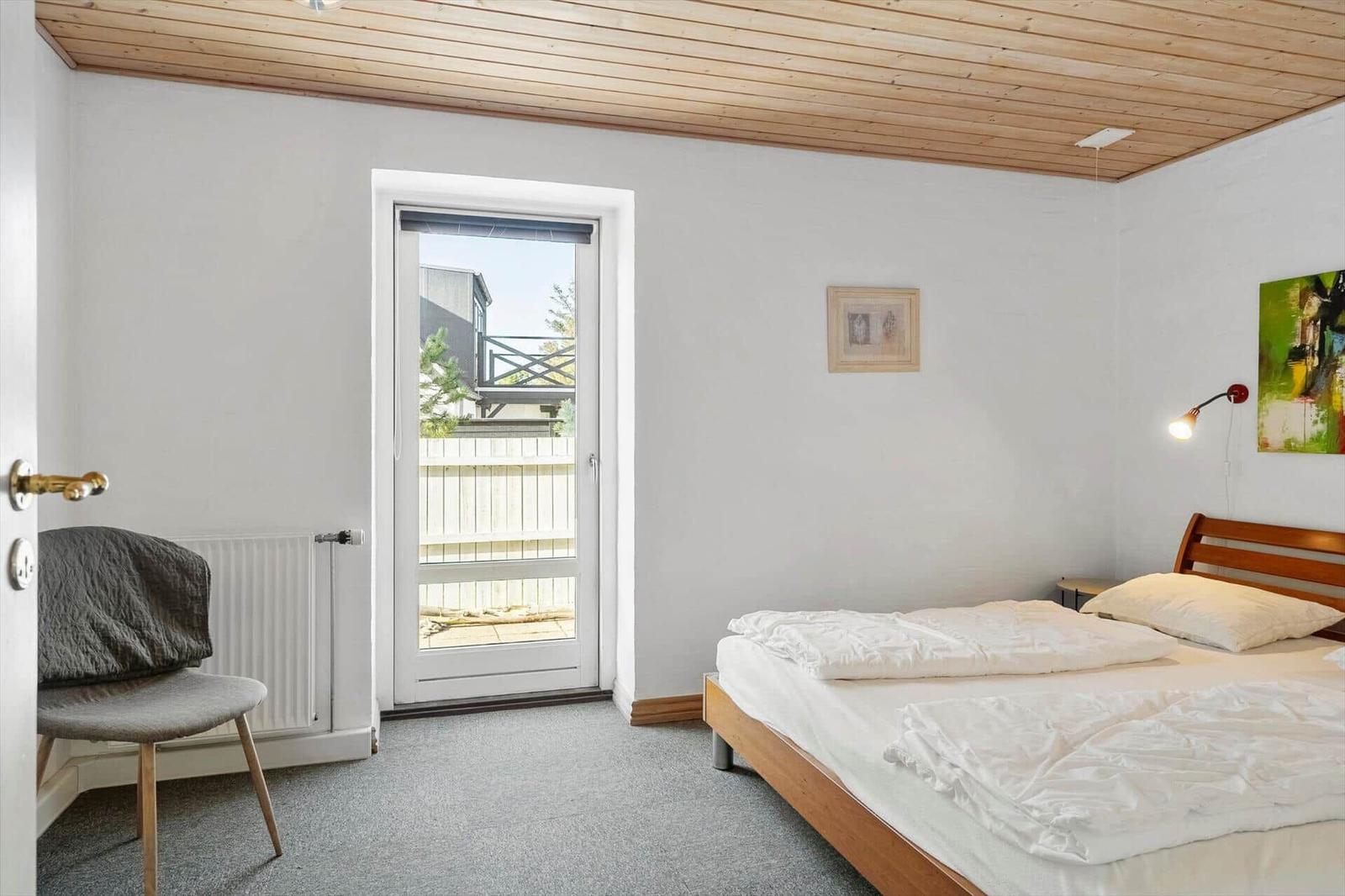 Bedroom with bed, door to balcony, and wooden ceiling.