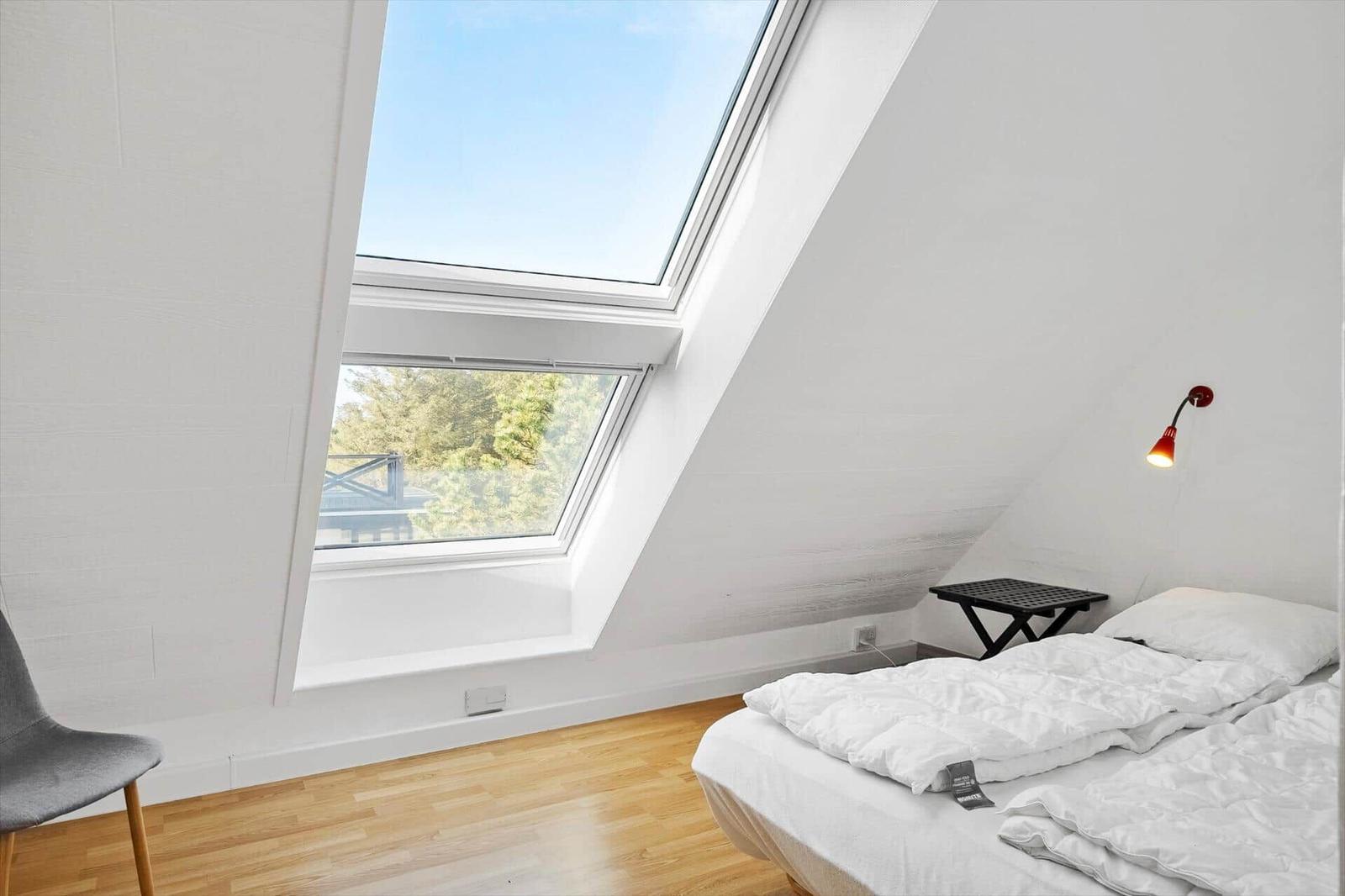 Bedroom with skylight, bed, and chair. Wooden floor and white walls.