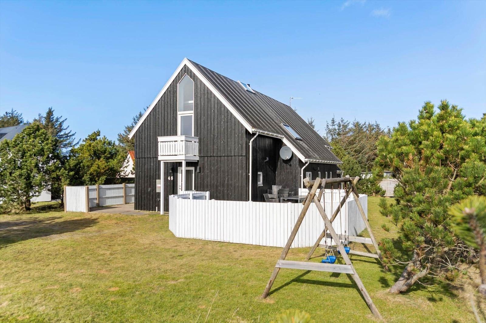 Black wooden house with white fence and swing in the garden.