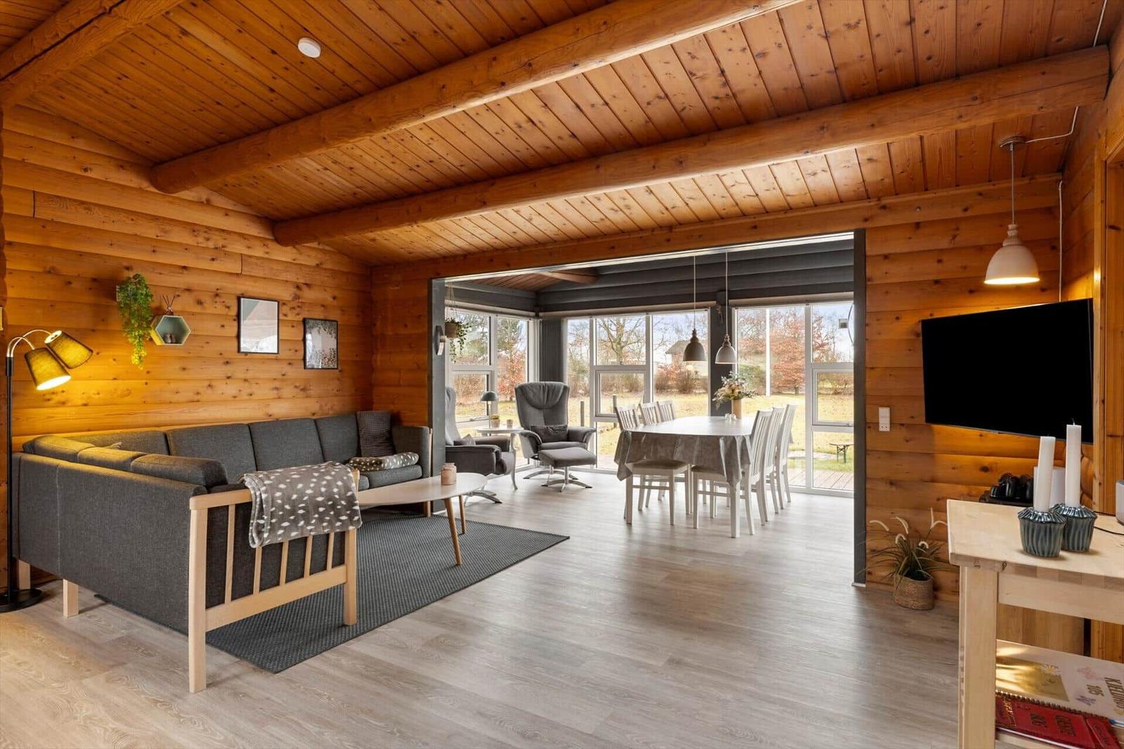 Wohn- und Essbereich mit Holzwand, Sofa, Tisch und großen Fenstern.