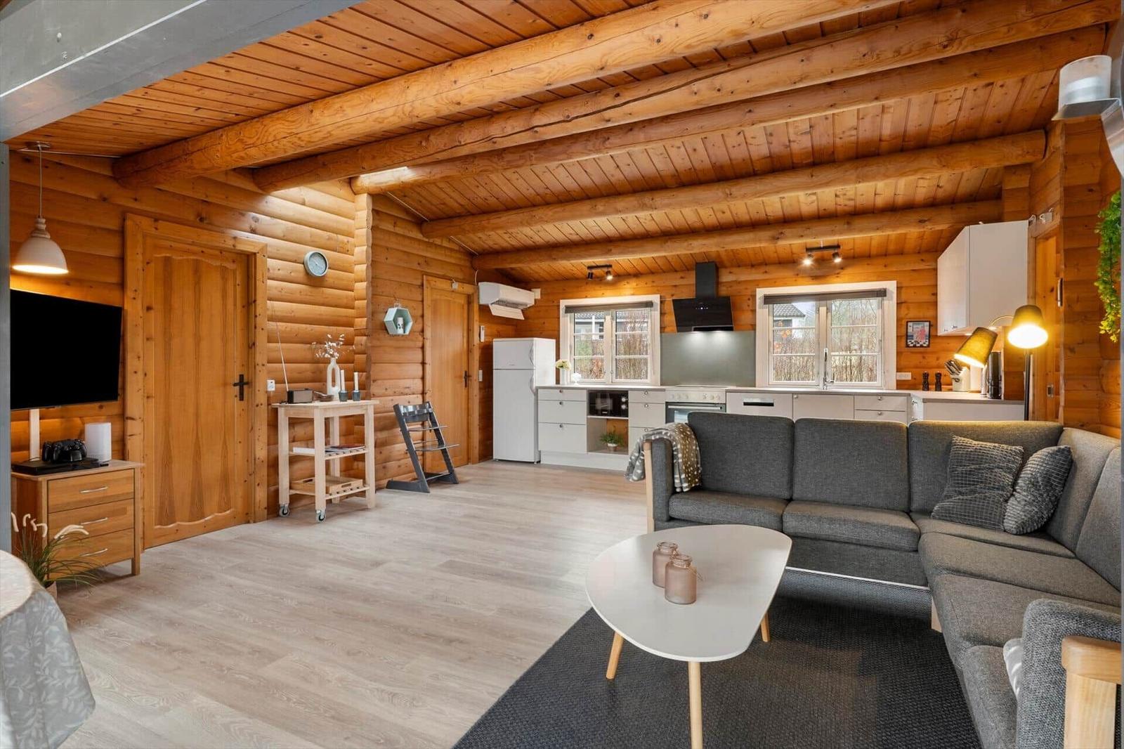 Wohnzimmer mit Küche und Holzdecke. Sofa, Couchtisch und Fernseher sichtbar.