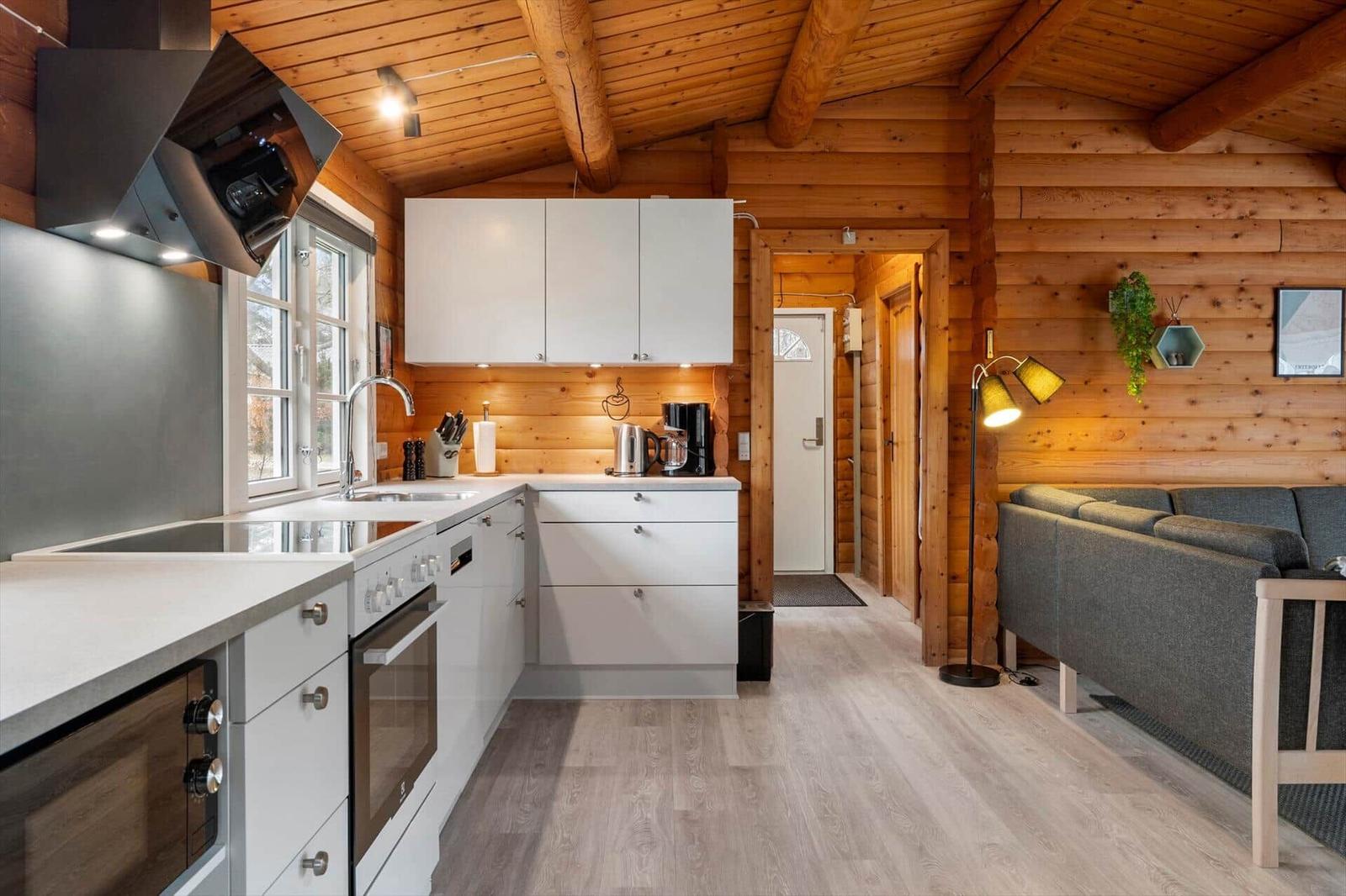 Küche mit weißen Schränken und Holzwand. Wohnbereich mit Sofa und Stehlampe.