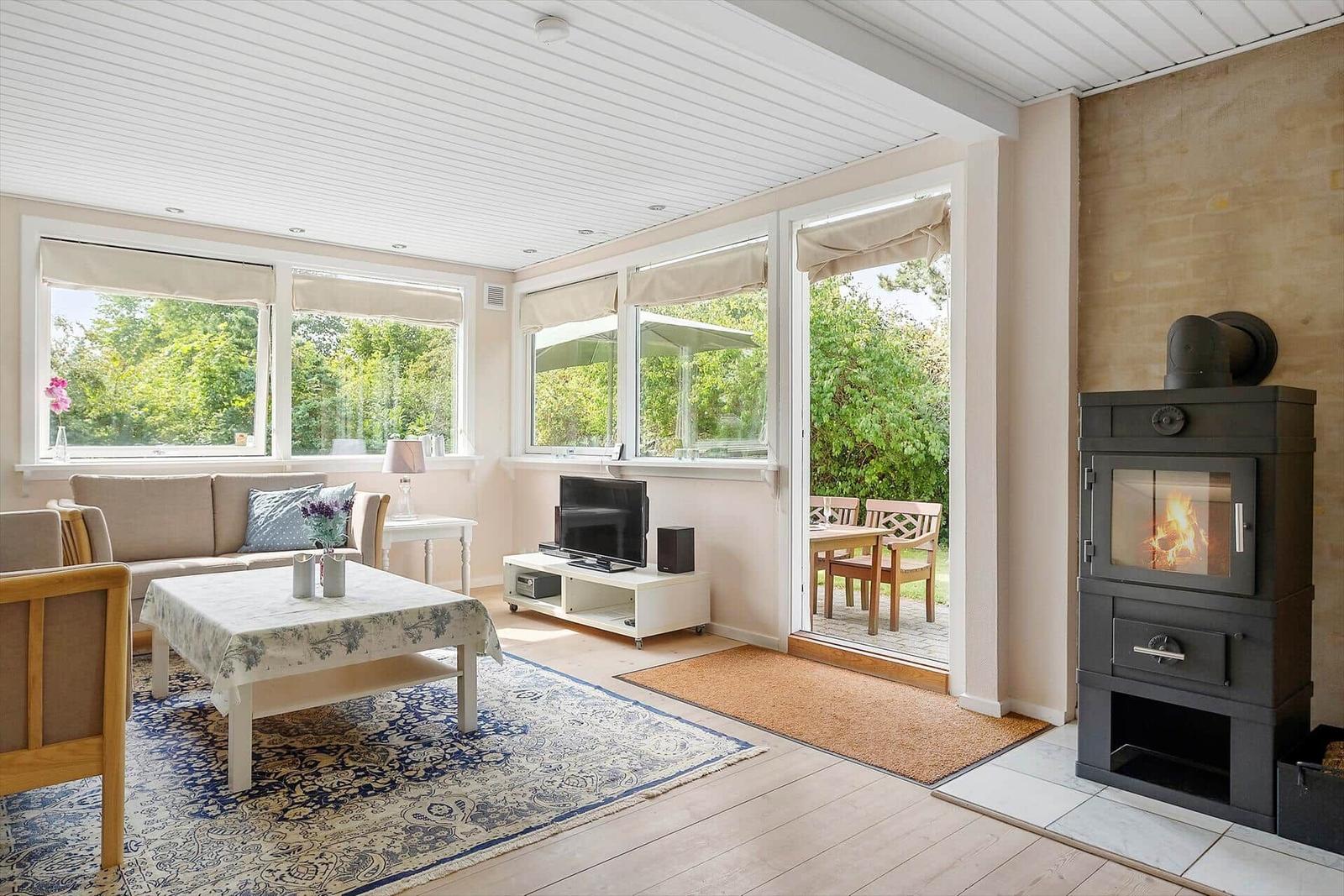 Wohnzimmer mit Kamin, Sofa, Fernseher und Blick auf Garten