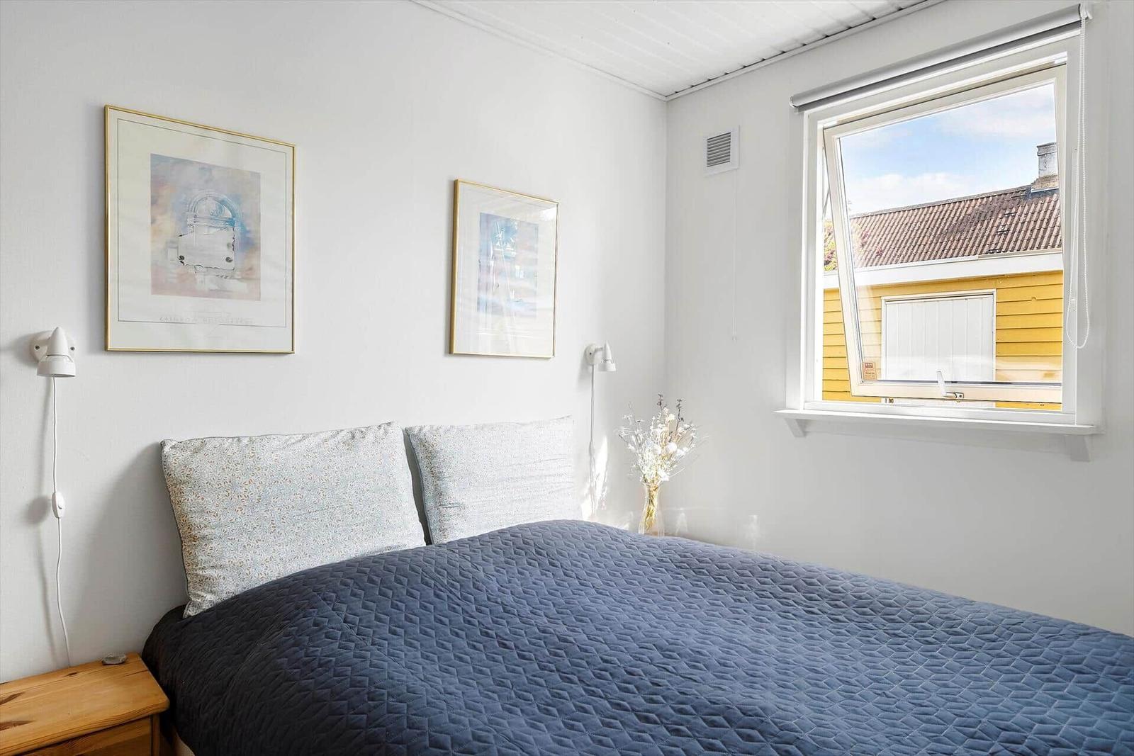 Schlafzimmer mit Bett, Fenster und Wandbildern.