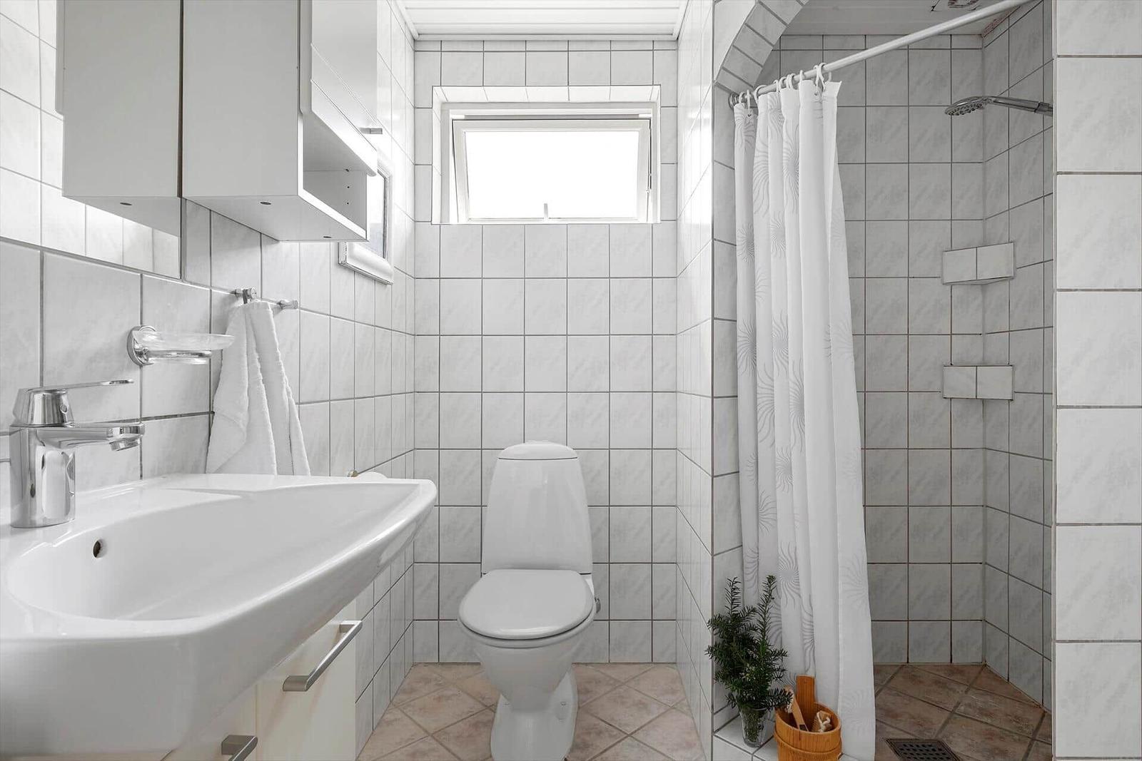 Badezimmer mit Dusche, Toilette und Waschbecken. Fliesenwand und Fenster.