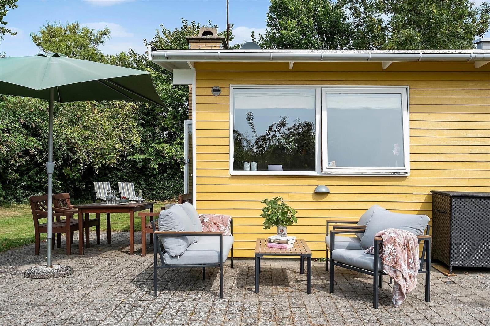 Terrasse mit Sitzgruppe, Tisch und Sonnenschirm vor gelbem Haus