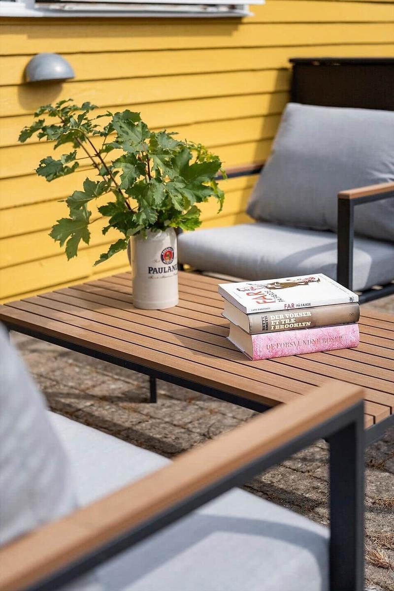 Terrasse mit Holztisch, Sitzmöbeln, Pflanze und Büchern.