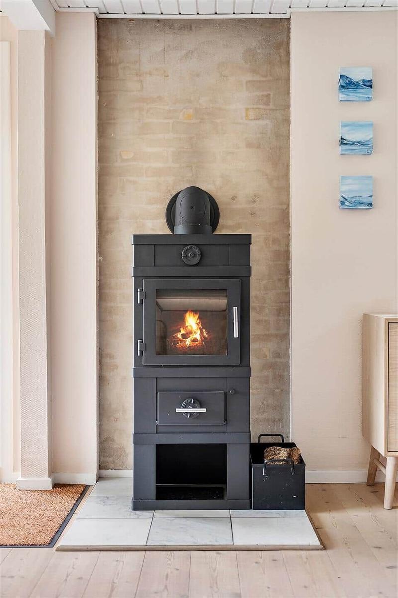 Holzofen mit brennendem Feuer in einem Raum mit Steinwand und Wandbildern.