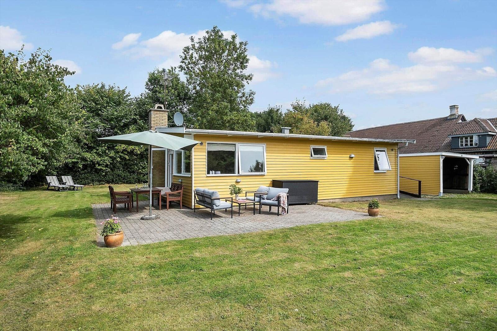 Gelbes Haus mit Terrasse, Garten und Sitzgelegenheiten unter Sonnenschutz.