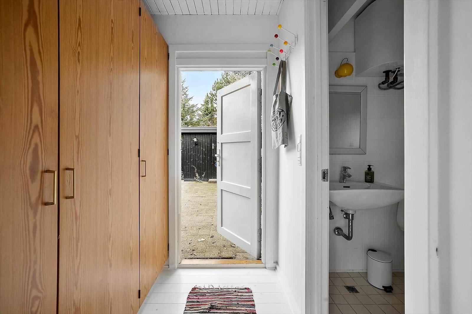 Hausgang mit Holzschrank, offener Tür zum Garten und Bad mit Waschbecken.