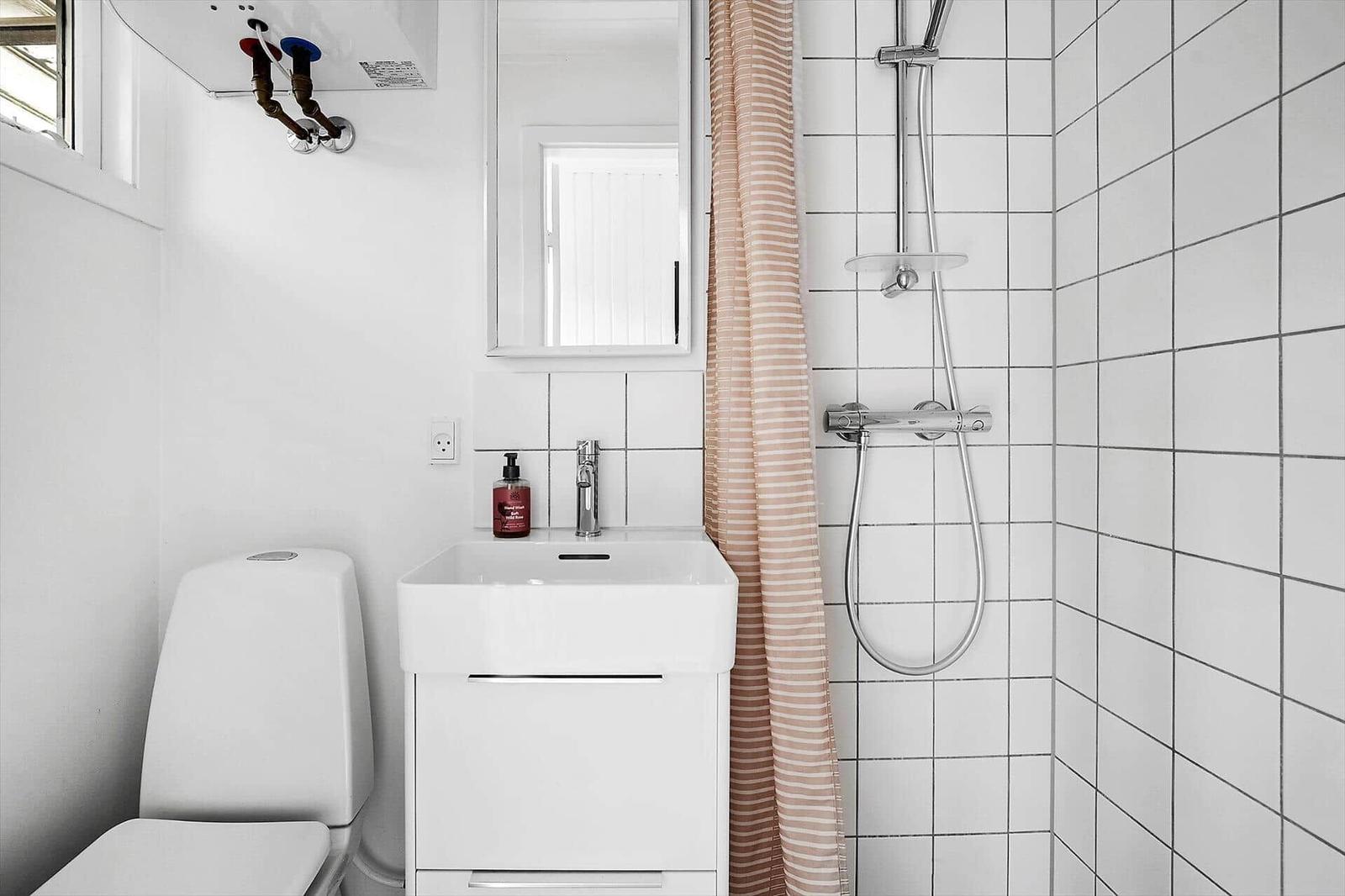 Badezimmer mit Dusche, Waschbecken und Toilette. Weiße Fliesen und rosa Streifentuch.
