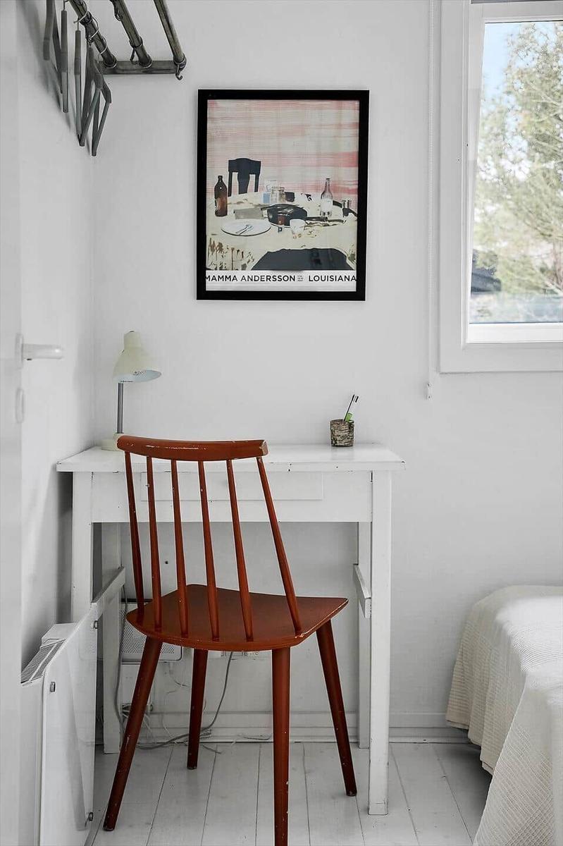 Schreibtisch mit Stuhl und Wandbild in einem hellen Raum mit Fenster.