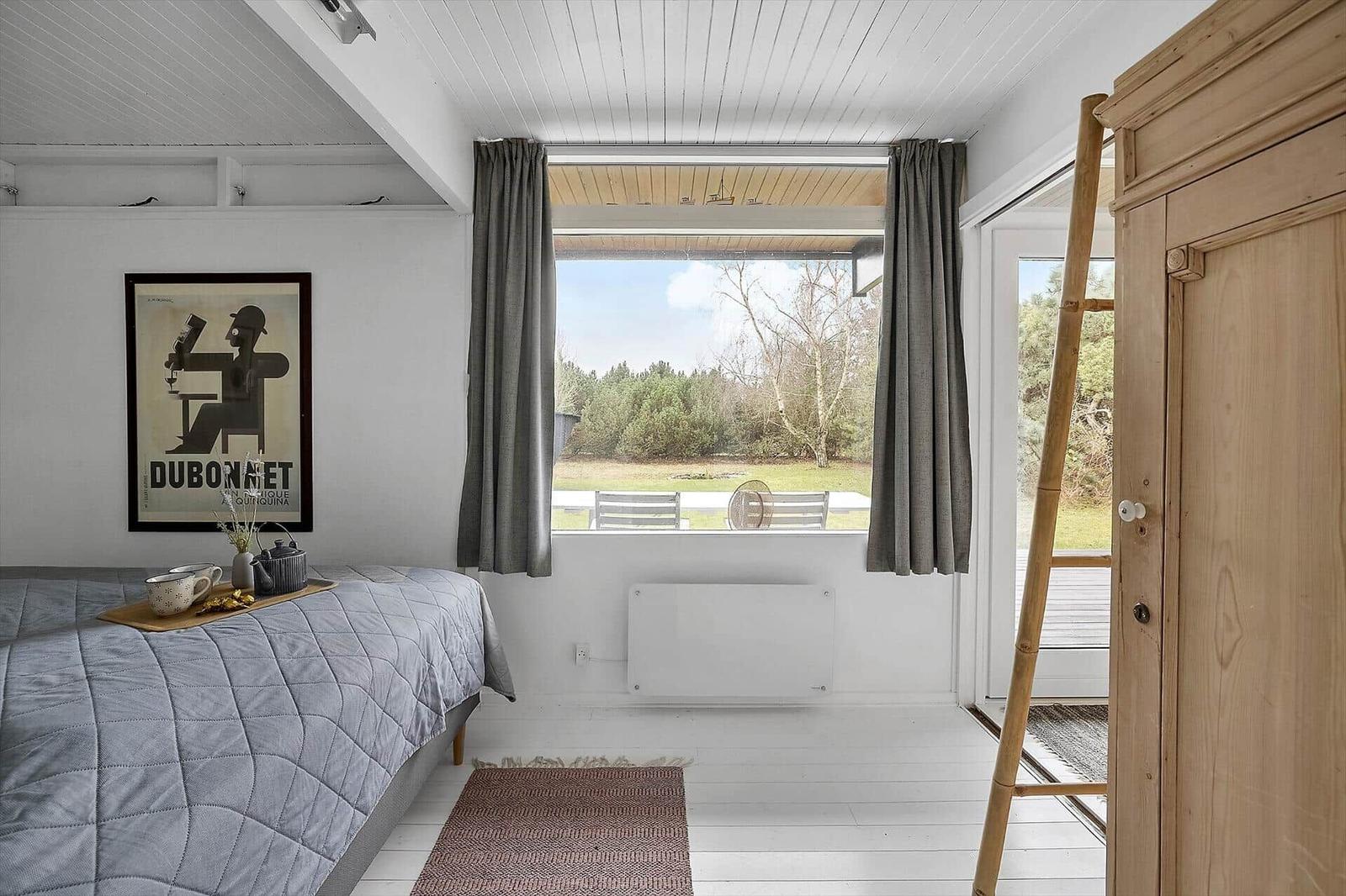 Schlafzimmer mit Bett, Fenster und Holzregal. Blick auf Garten.