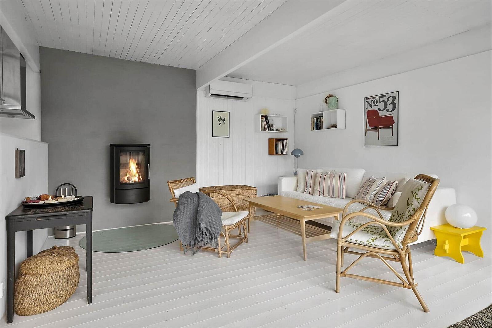 Wohnraum mit Kamin, Sofa und Stühlen. Weiße Wände und Holzboden.