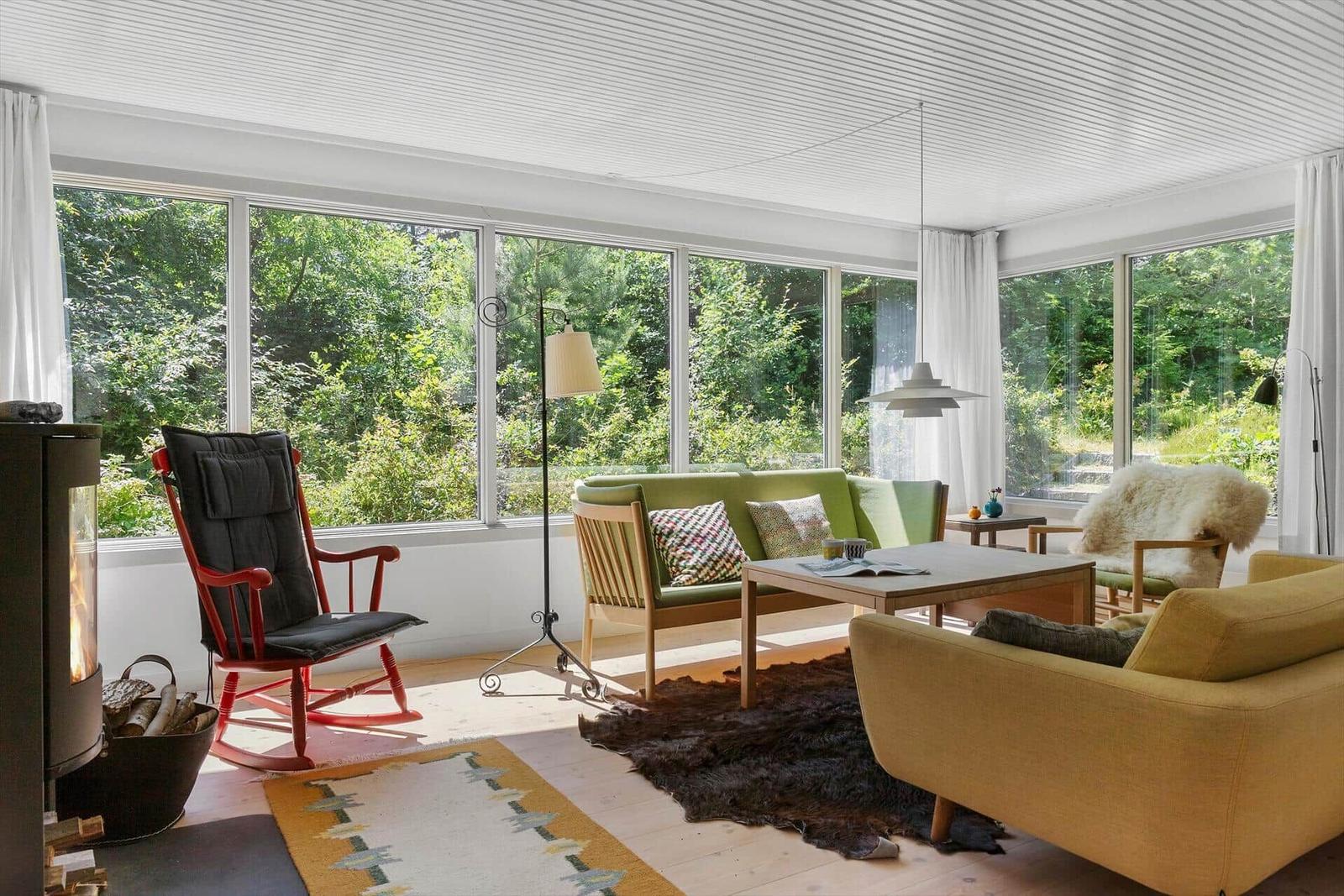 Ein Wohnzimmer mit großem Fenster, grünem Sofa, rotem Schaukelstuhl und Holzfußboden.