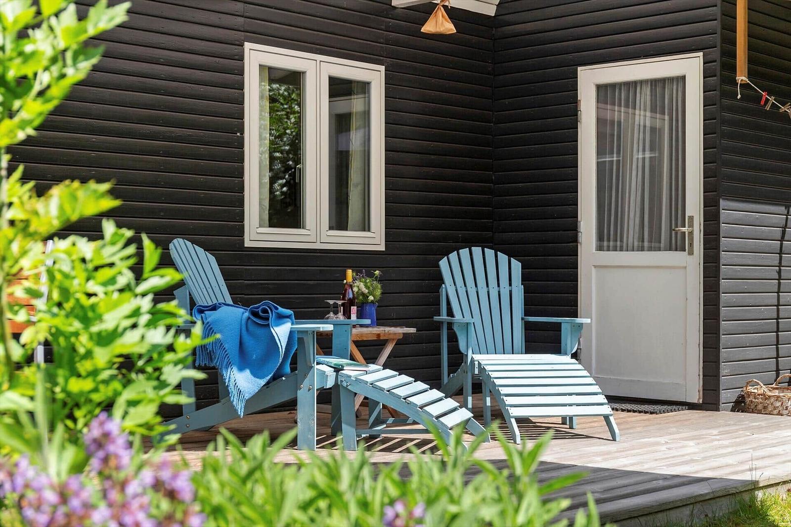 Terrasse mit blauen Stühlen, Tisch und Blumen vor schwarzem Holzhaus.