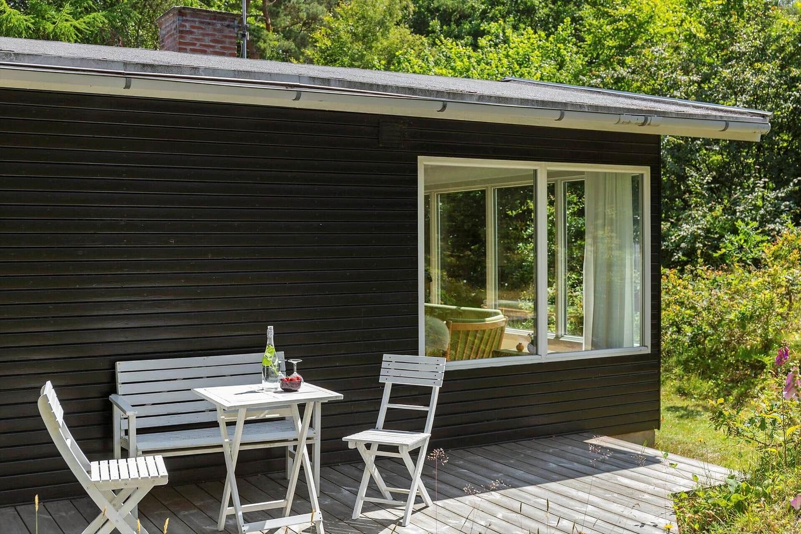 Schwarzes Holzhaus mit Terrasse, weißem Tisch und Stühlen, grüne Umgebung