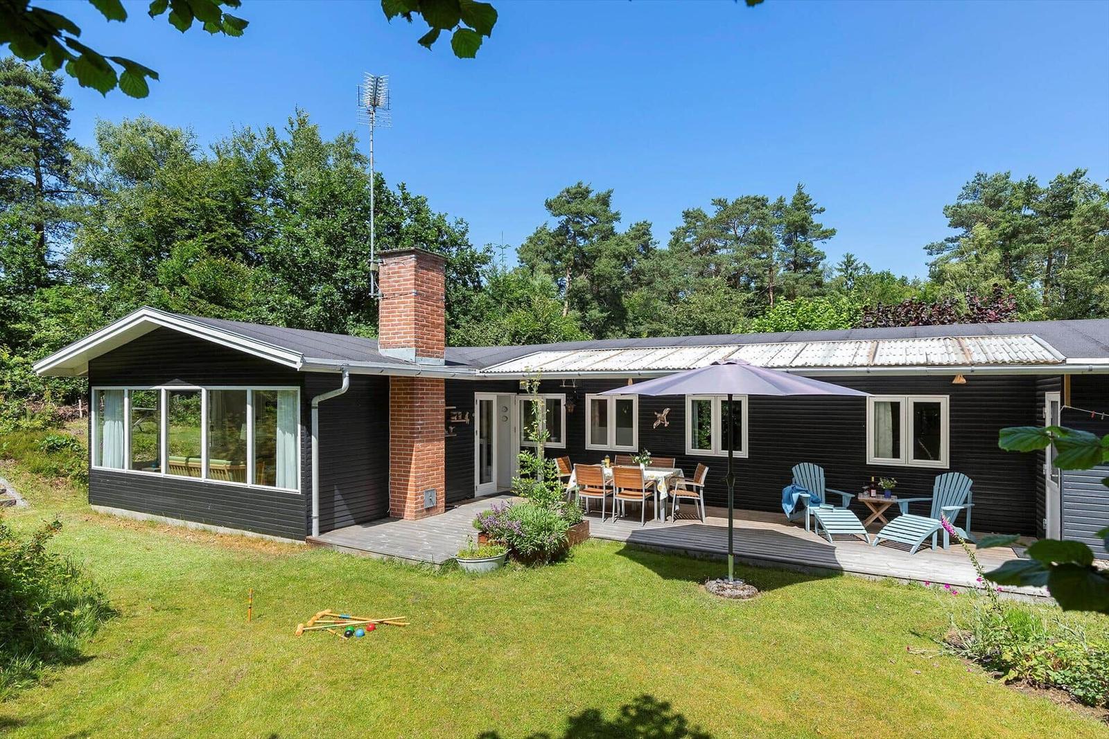 Schwarze Holzhütte mit Terrasse, Garten und Grillplatz im Wald.