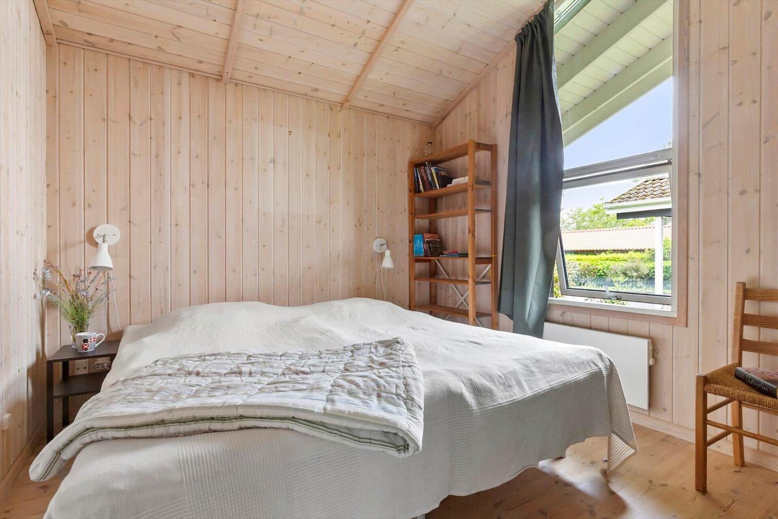 Schlafzimmer mit Holzwand, Bett, Bücherregal und Fenster mit Blick.