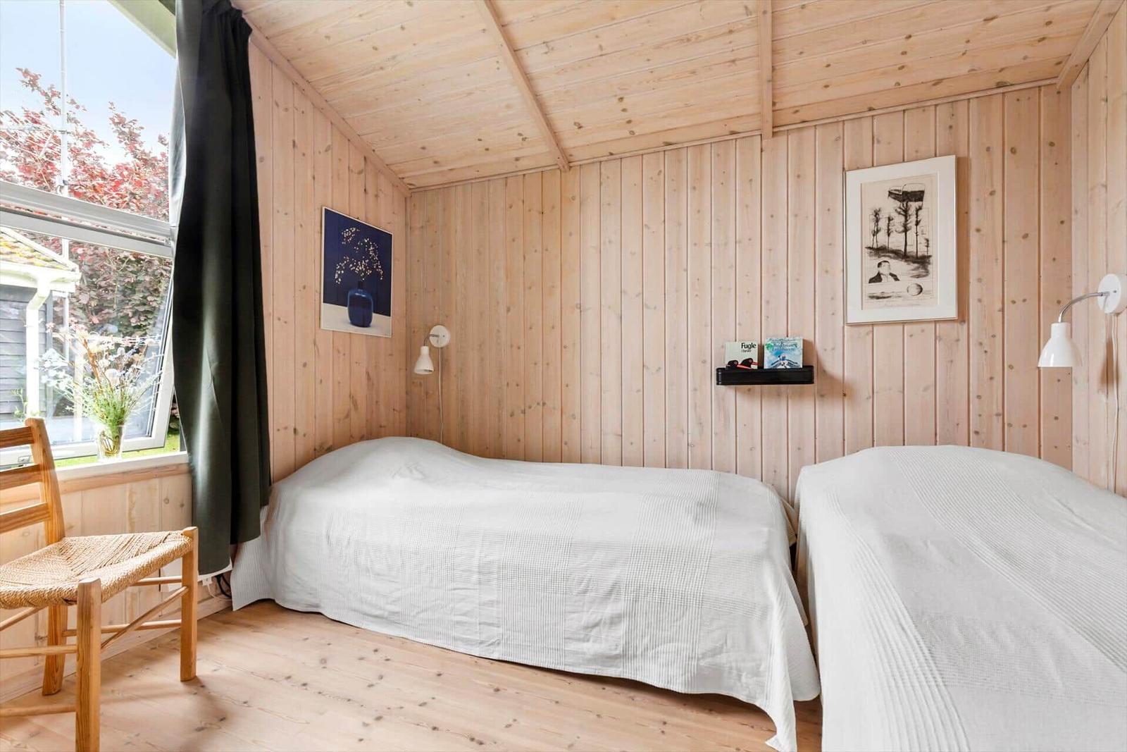 Zwei Betten in einem Holzhauszimmer mit Fenster und Stuhl.