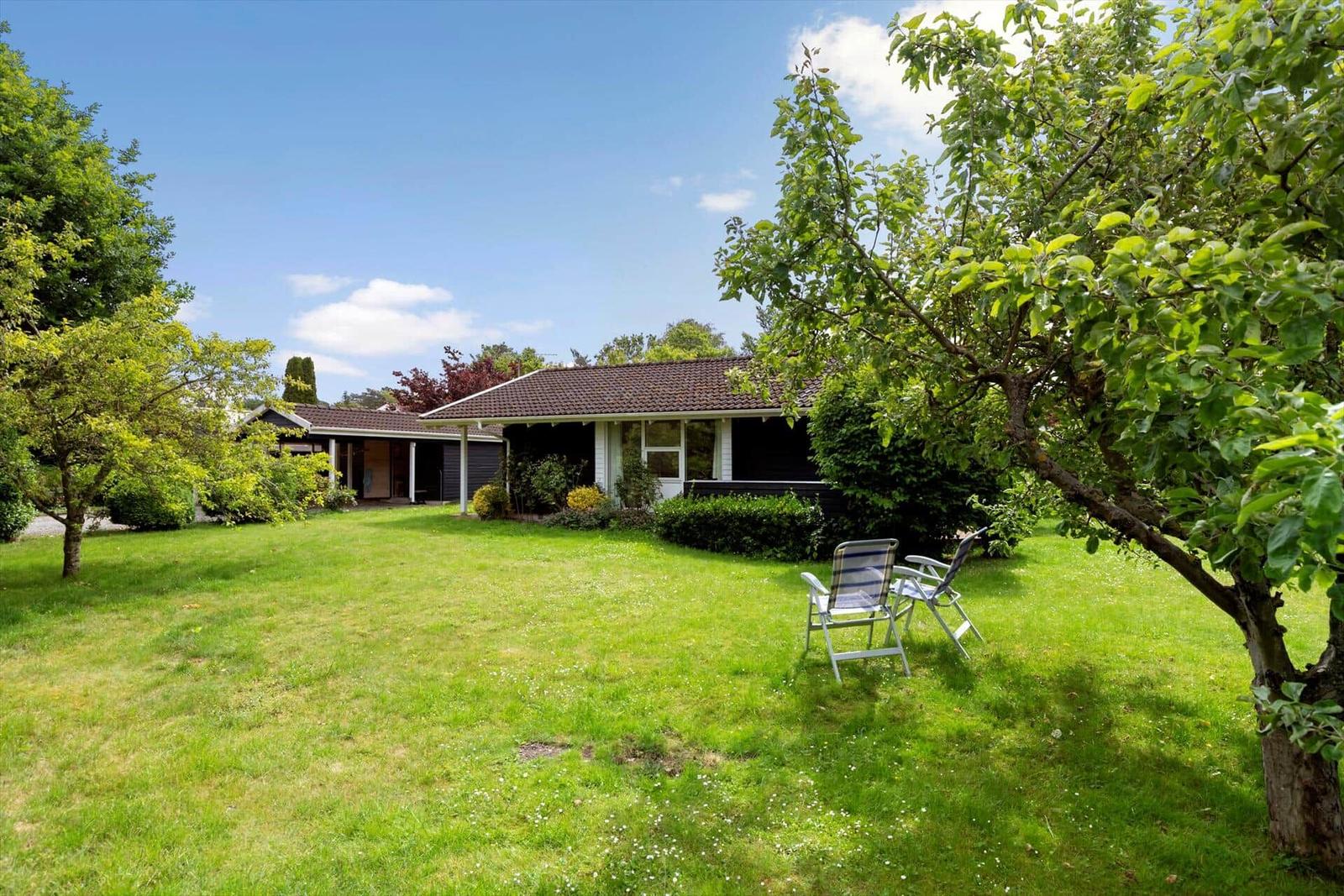 Haus mit großem Garten, Sonnenliegen und Bäumen unter blauem Himmel.