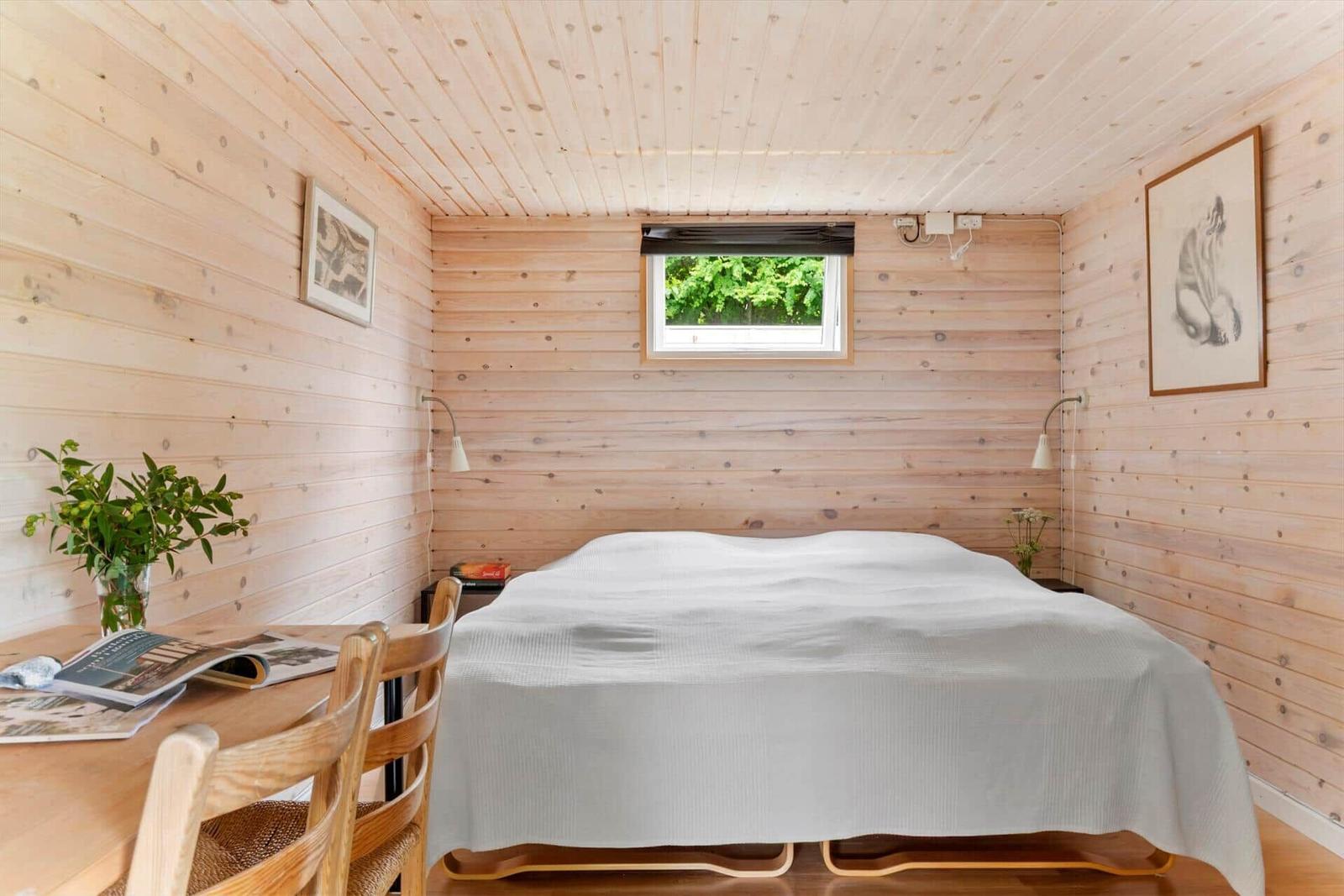 Schlafzimmer mit Holzwand, Bett, Tisch und Fenster.