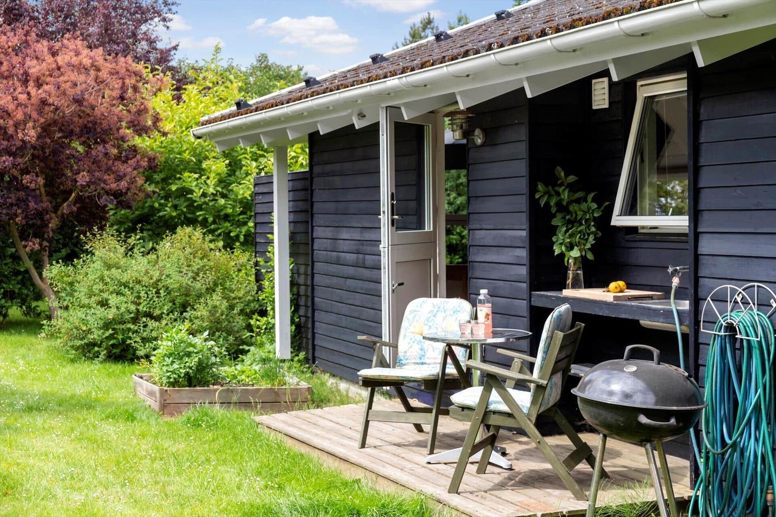Hütte mit Terrasse, Grill und Garten. Holzterrasse mit Stühlen und Tisch.
