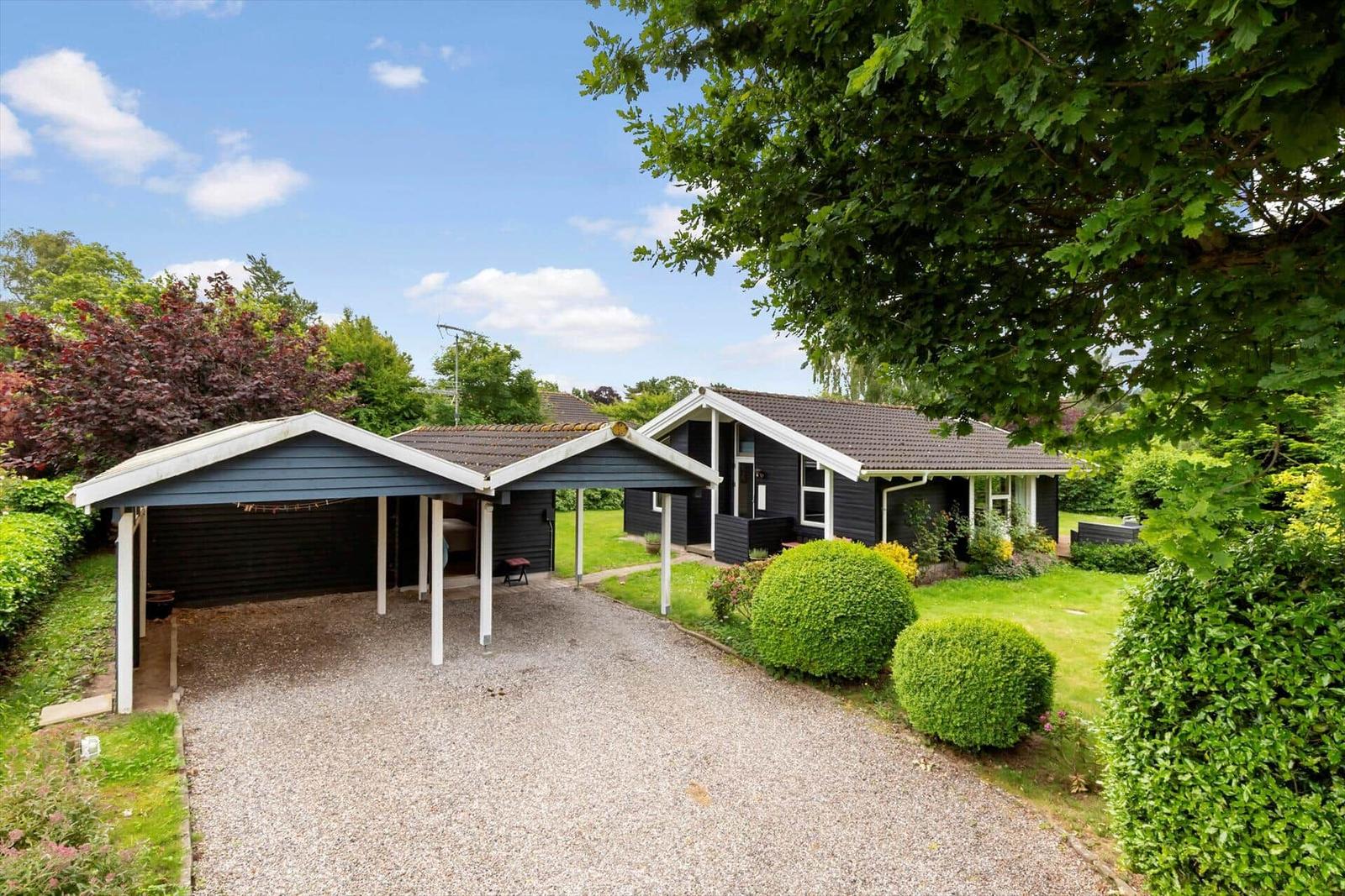 Schwarzes Haus mit Carport, Grasfläche und Bäumen.