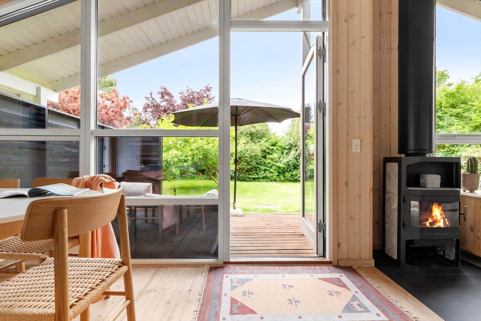 Raum mit Holzfußboden, Kamin und Terrassentür zur grünen Außenterrasse.