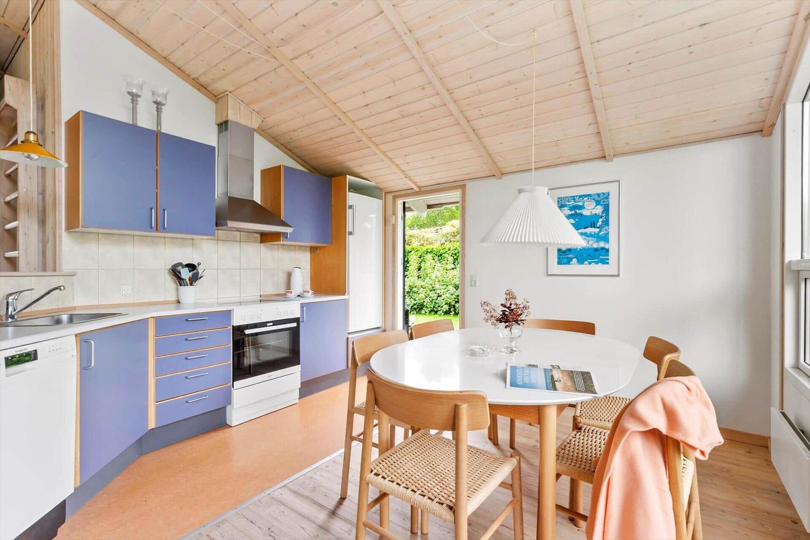 Küche mit Essbereich unter Holzdecke, blau lackierte Schränke und runde Tischplatte.