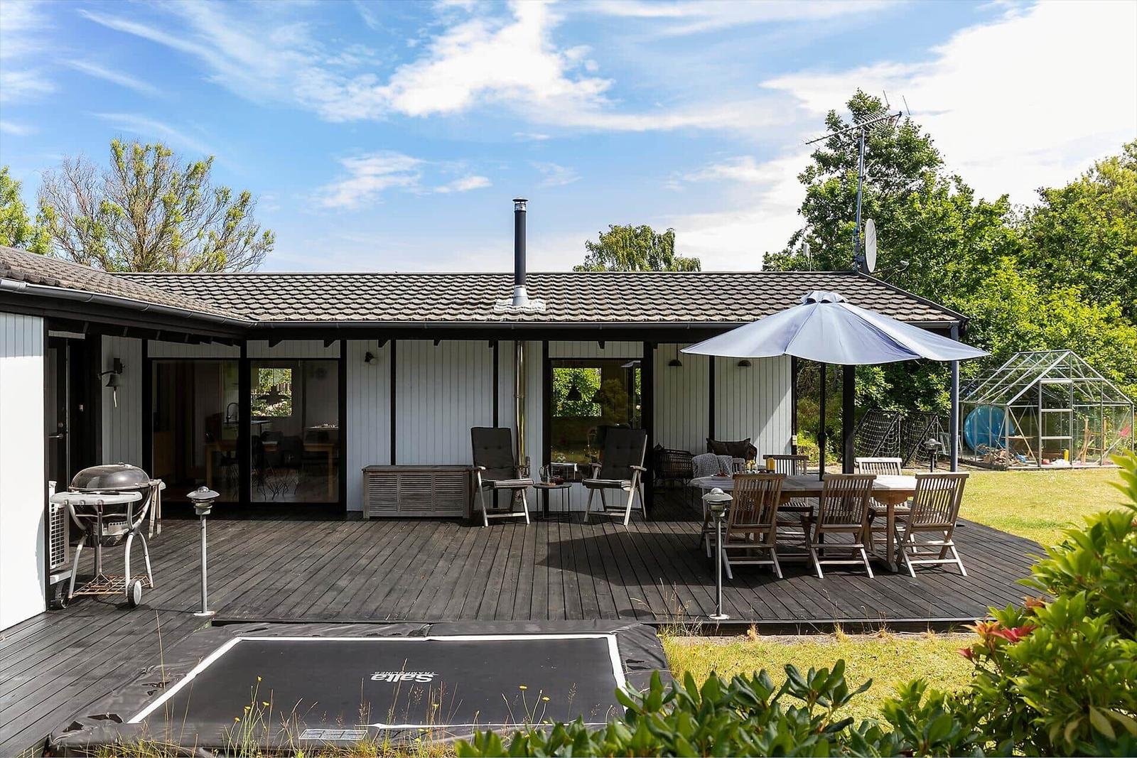 Haus mit Terrasse, Grill und Sitzgruppe unter Sonnenschutz.
