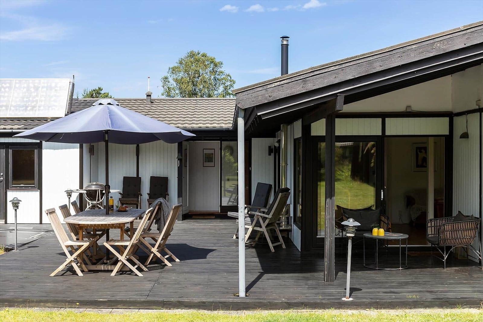 Terrasse mit Tisch, Stühlen und Sonnenschirm. Sicht auf Wohnbereich und Garten.