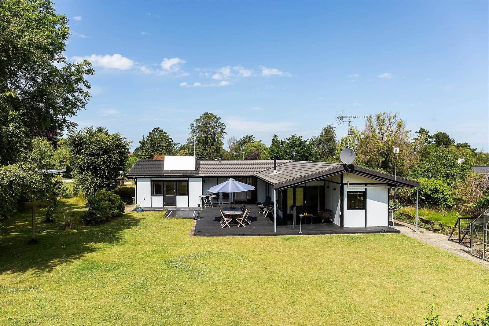 Ein Haus mit Terrasse, Garten und Sonnenschirm unter blauem Himmel.