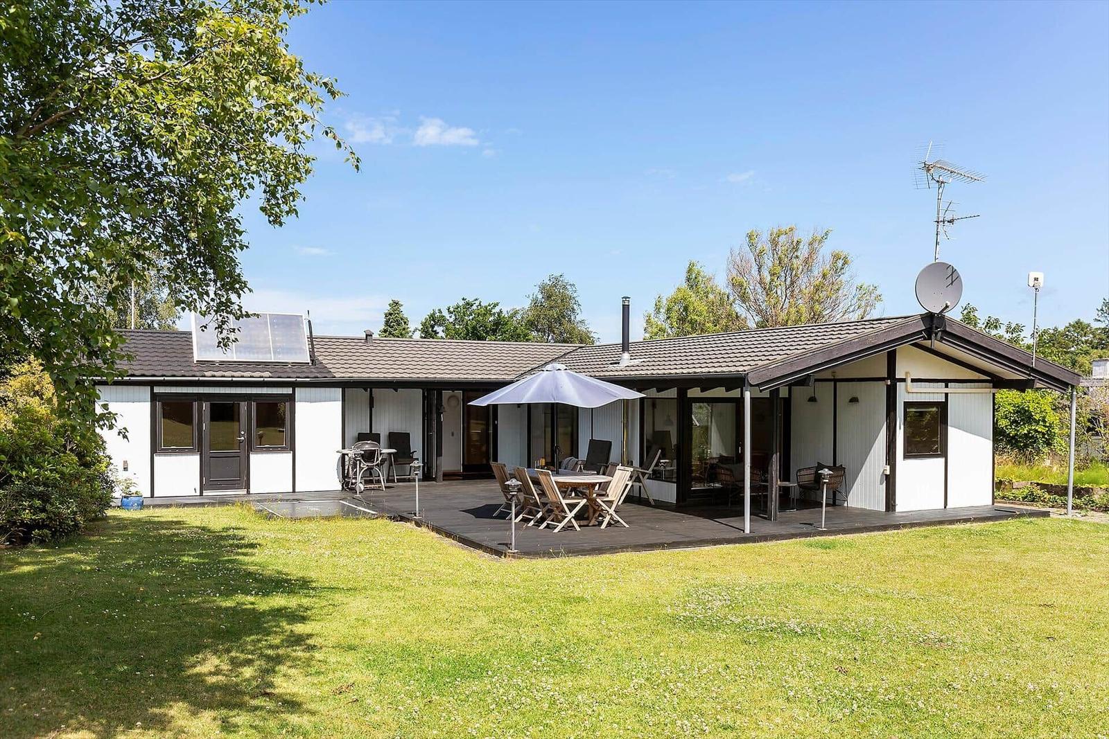Ein Haus mit Terrasse, Garten und Sonnenschirm. Satellitenschüssel und Antenne sind sichtbar.