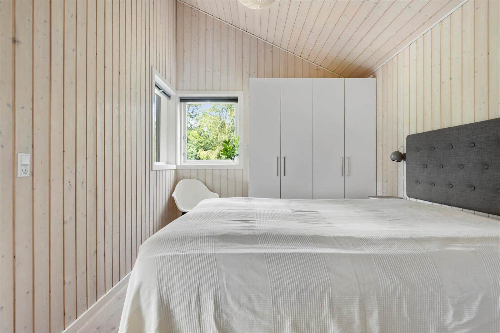 Schlafzimmer mit Holzwand, Bett, Schrank und Fenster.
