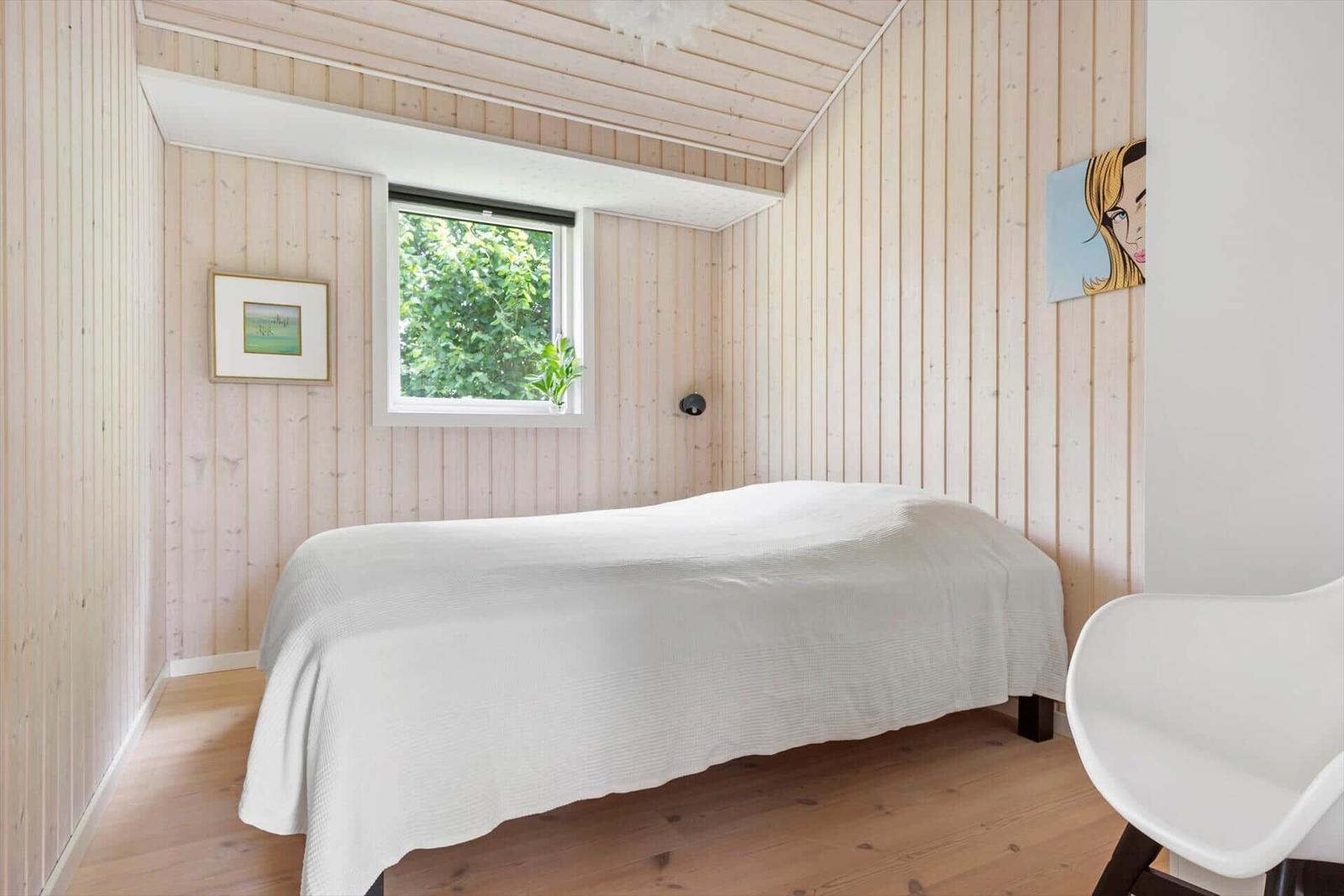 Schlafzimmer mit Holzwand, Bett und Fenster mit Blick auf Grün.