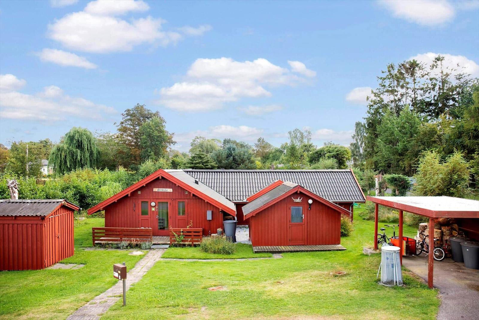 Roter Holzhauskomplex mit Garten und Fahrradabstellplatz unter blauem Himmel.