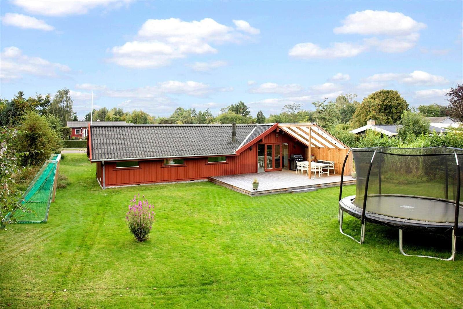 Rotes Haus mit Terrasse, Grill und Trampolin im Garten.