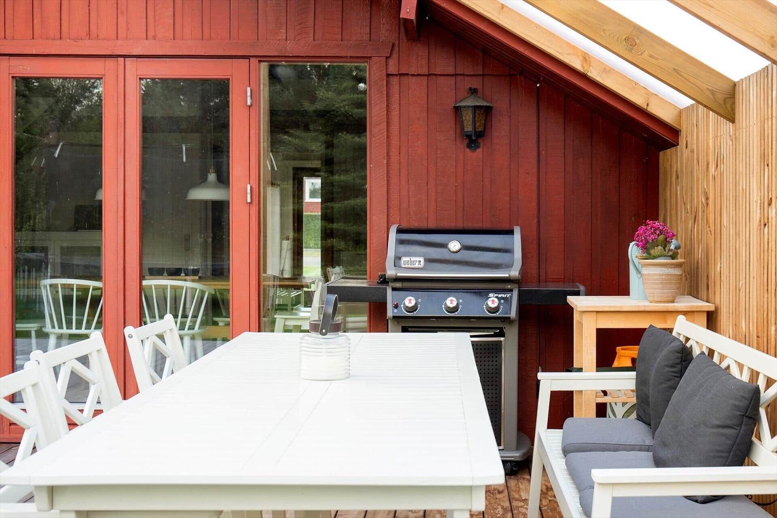 Roter Holzausenaufenthalt mit Grill, Tisch und Bank.