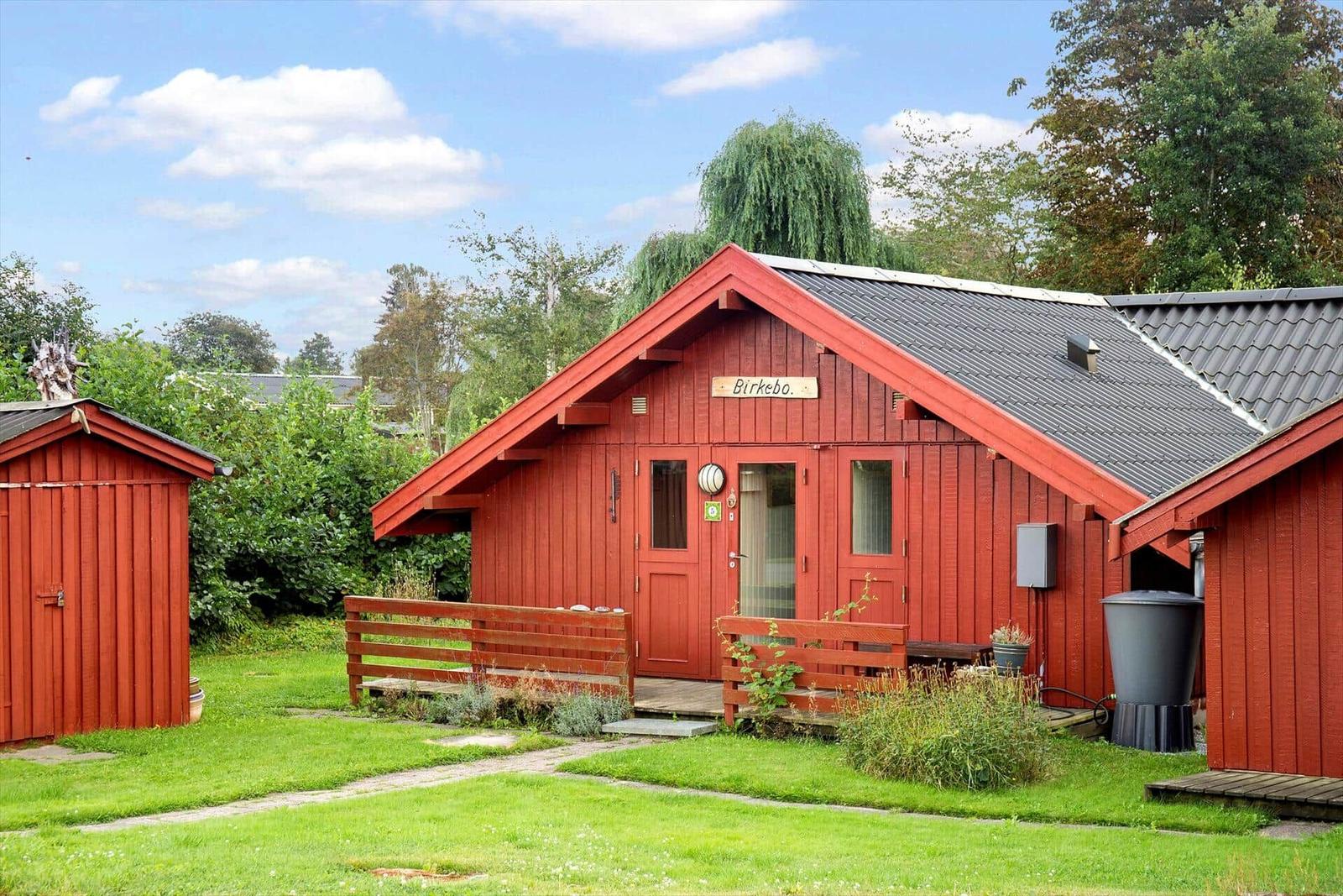 Rotes Holzhaus mit Garten und Holzbank vor der Tür.