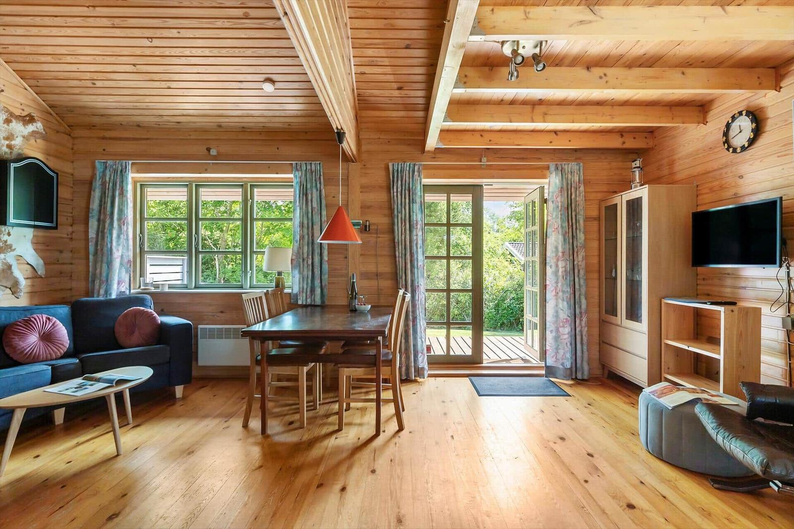 Holzvertäfelte Wohnung mit Essbereich, Sofa und TV. Durchgang zur Terrasse.