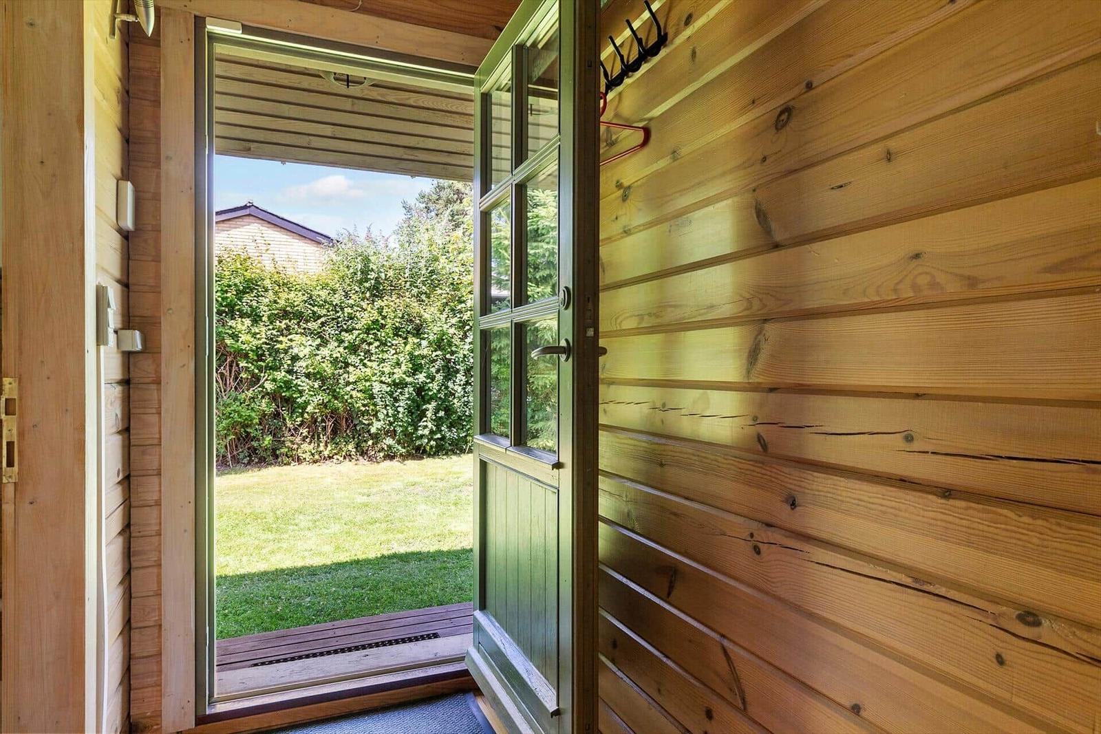 Holzverkleidete Türöffnung zum Garten mit Rasen und Hecke.