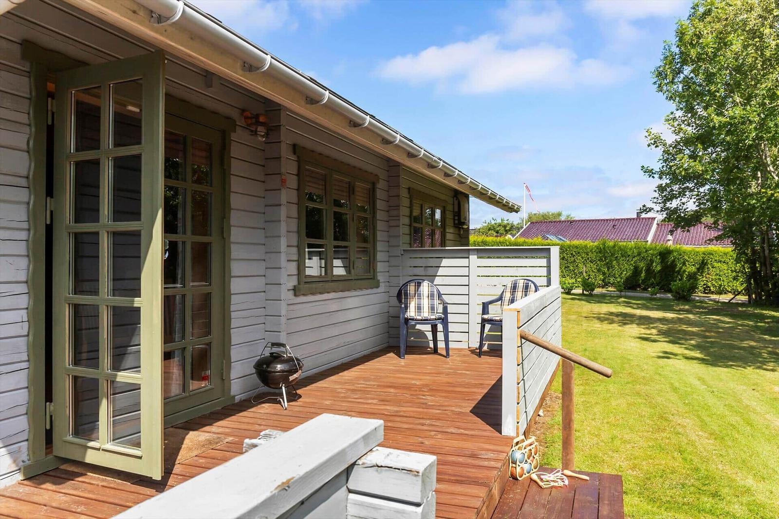 Terrasse mit Grill und Stühlen vor einem Haus mit Holzfassade.