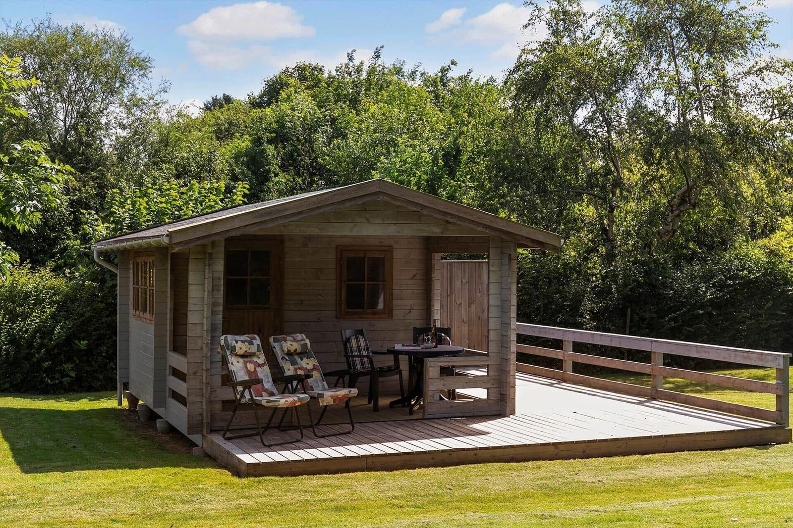 Holzhütte mit Terrasse, Gartenmöbeln und Blick auf Bäume.