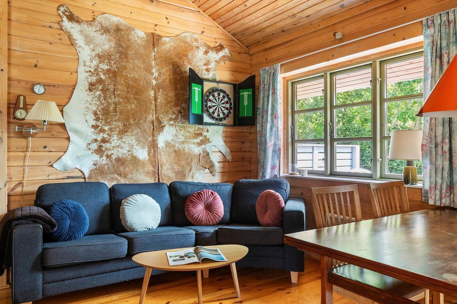 Wohnzimmer mit Sofa, Tisch und Dartboard an Holzwand
