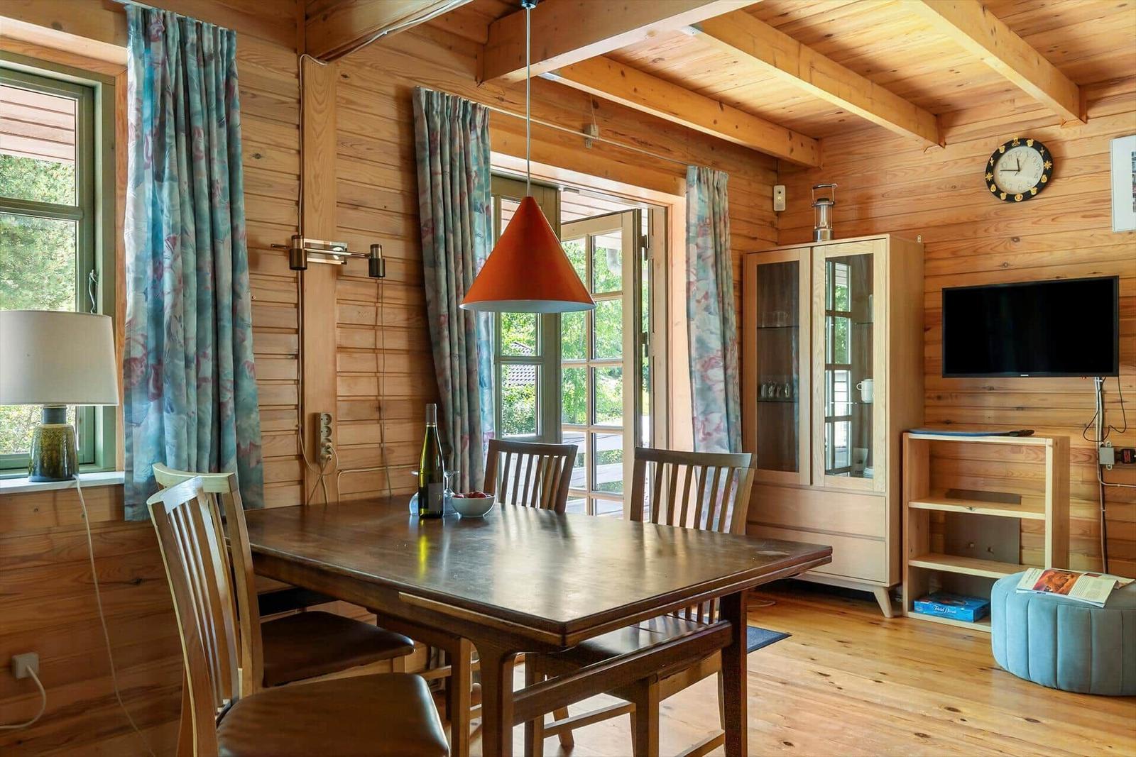Esszimmer mit Holztisch, Stühlen und Fensterblick. Wanduhr, TV und Schrank sind vorhanden.