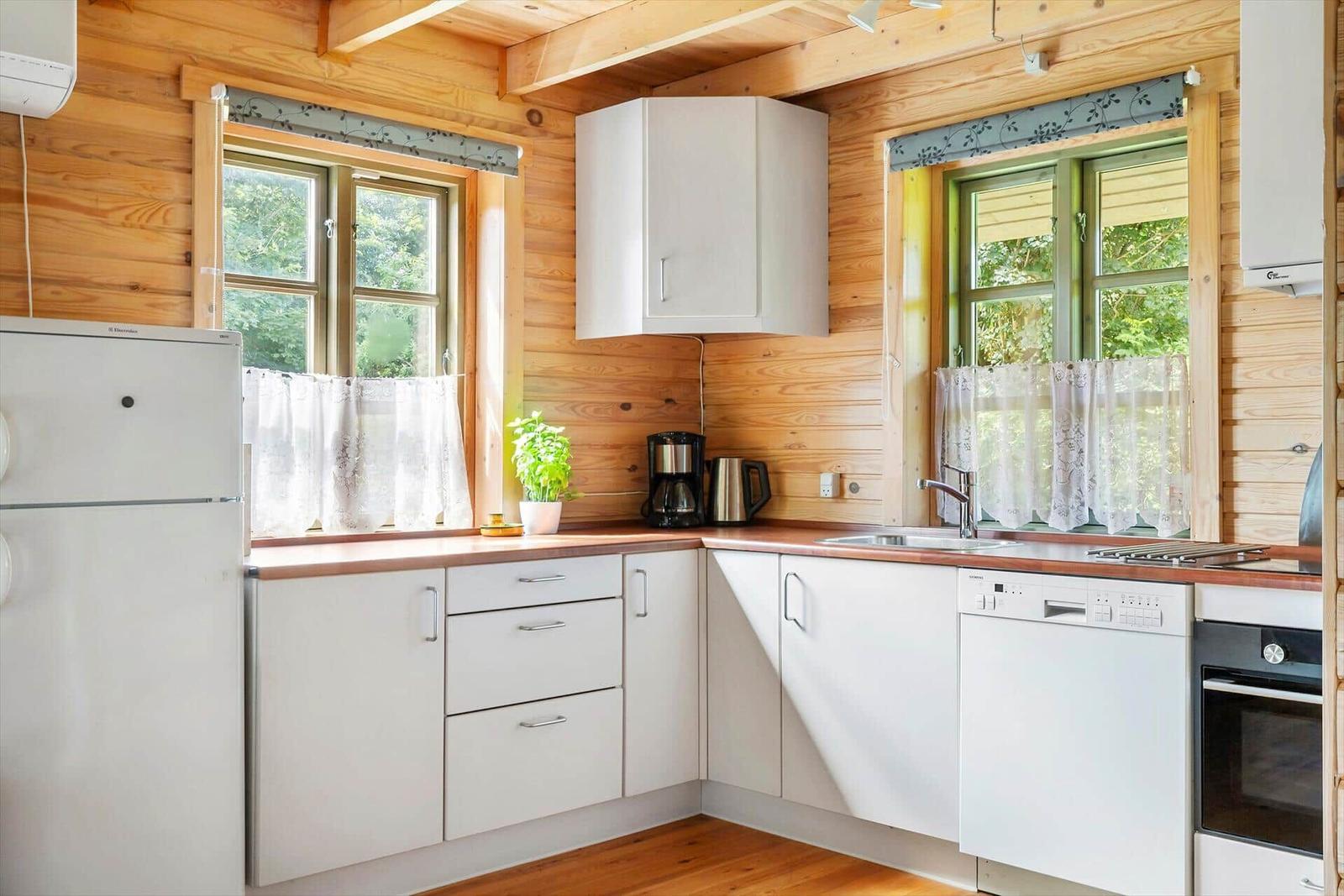 Küche mit weißen Schränken, Holzwänden und Fenstern mit Vorhängen.